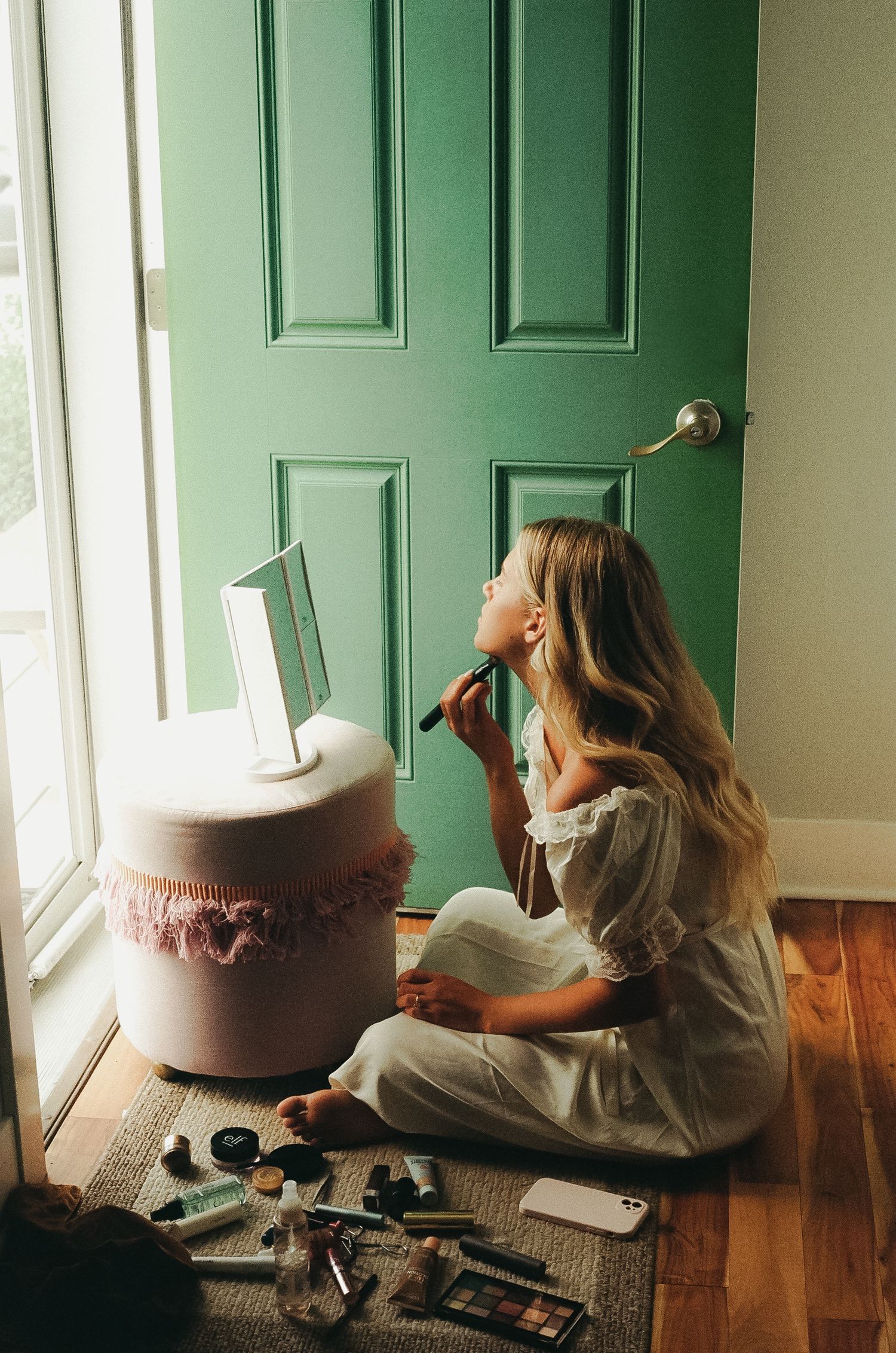 A person sits by a green door with a mirror and makeup supplies for preparation.