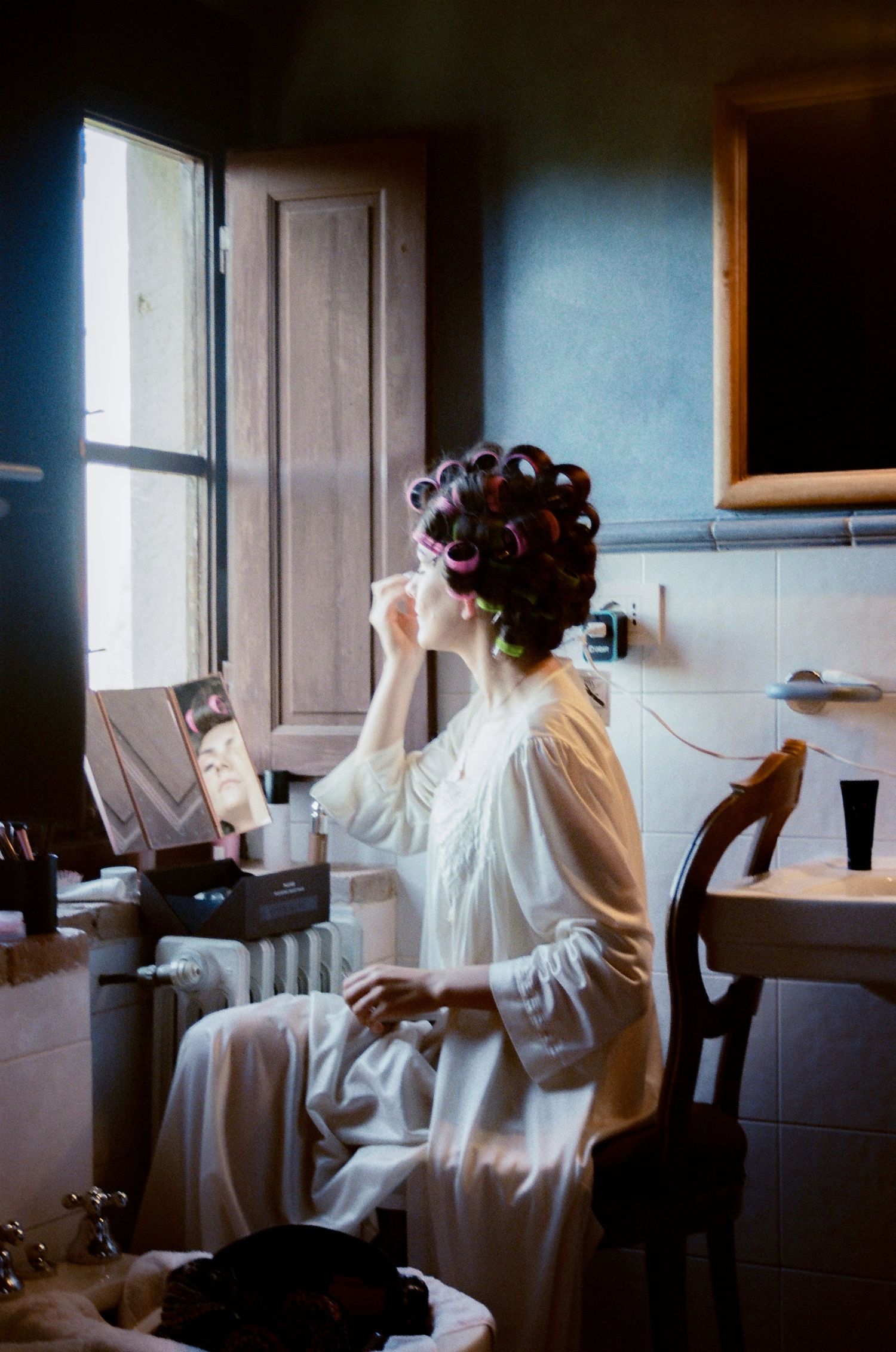 A series of photos showing someone in a white robe sitting by a window with hair curlers, creating a vintage aesthetic.