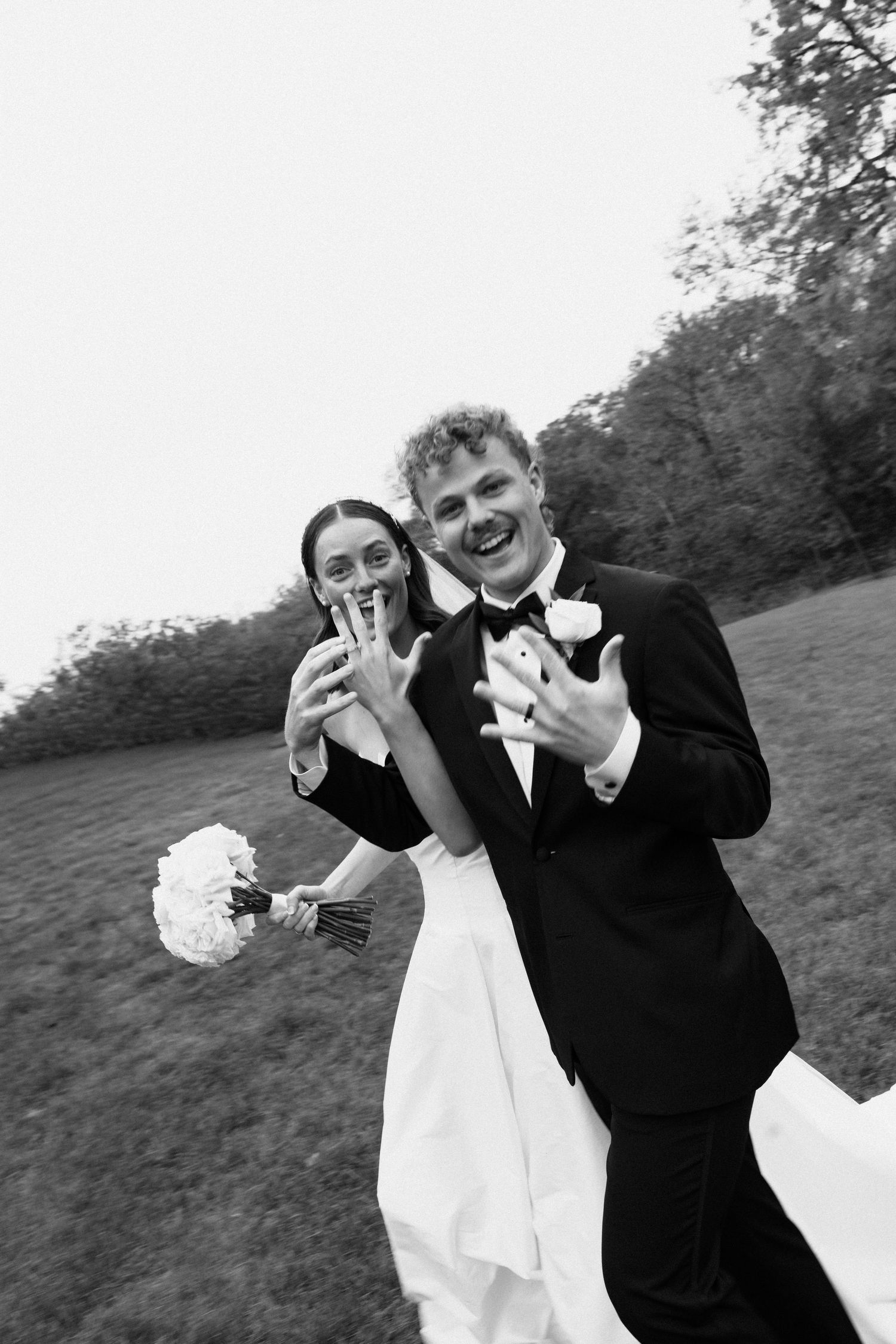 A bride and groom share a joyful candid moment together outdoors in black and white photography.