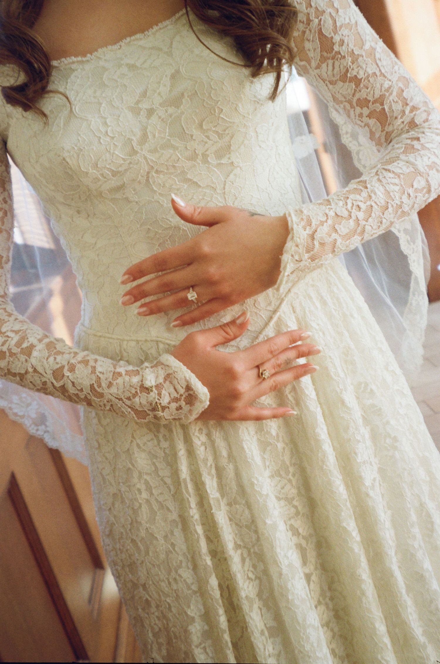 Close-up view of delicate white lace wedding dress details with long sleeves and intricate floral patterns.