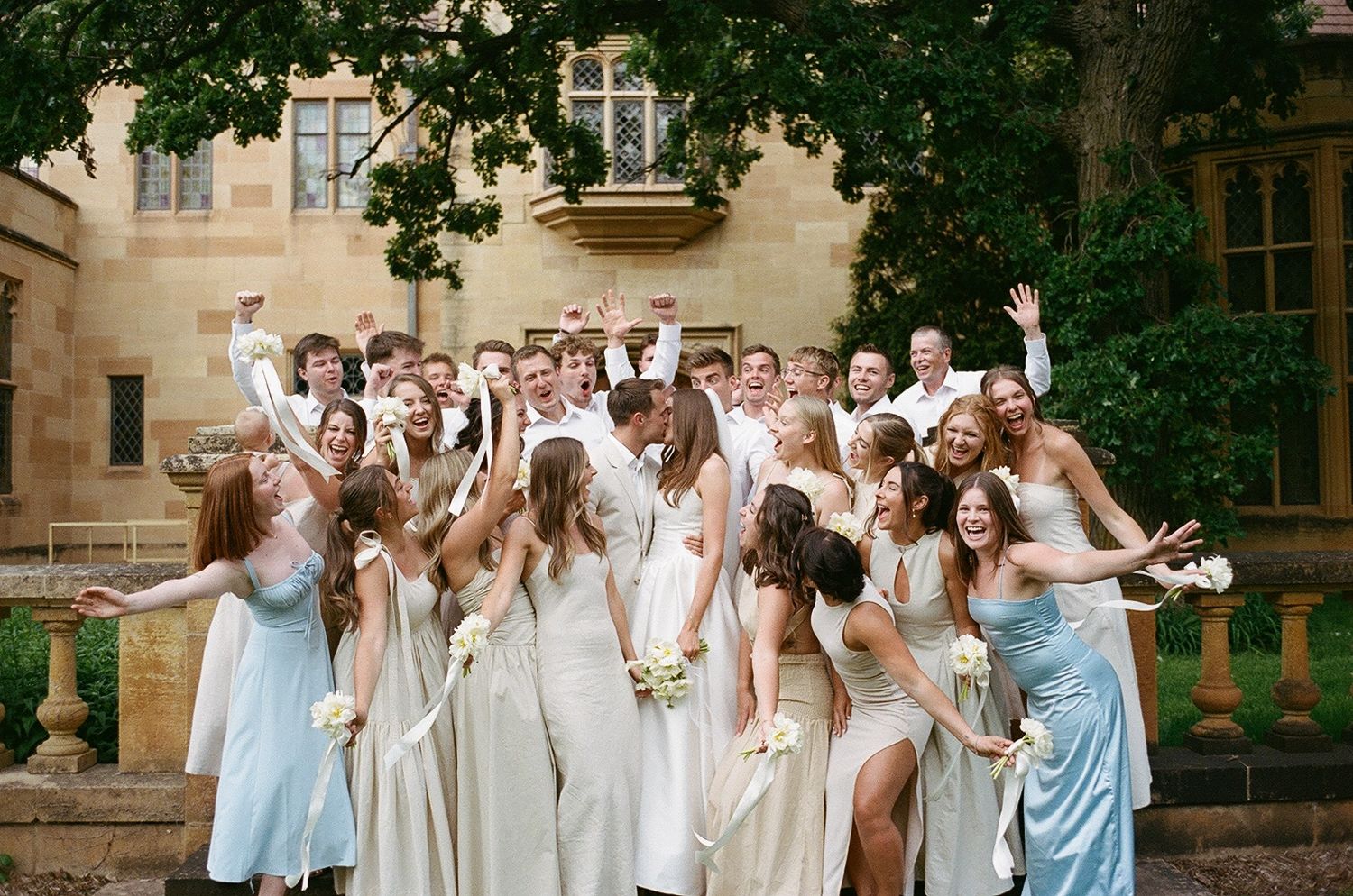 Wedding party in light blue and cream dresses celebrating joyfully on stone steps outdoors.