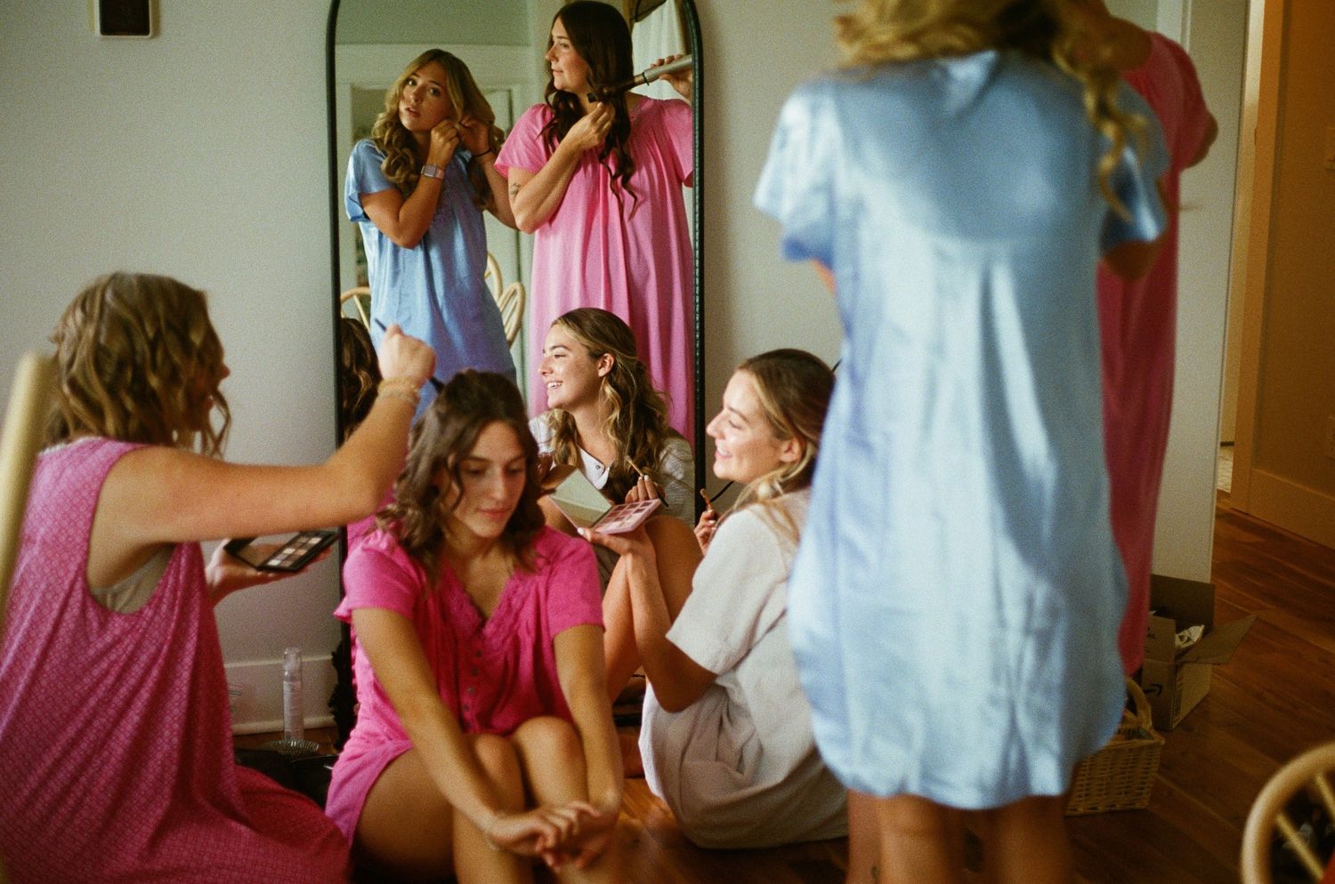 A group of bridesmaids in pink dresses gather in a hallway while getting ready for a wedding celebration.