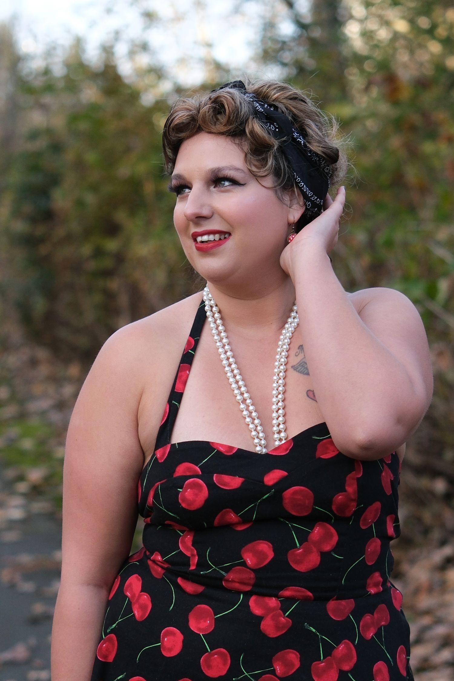 A woman with a vintage dress and hairstyle rests a hand on her hair