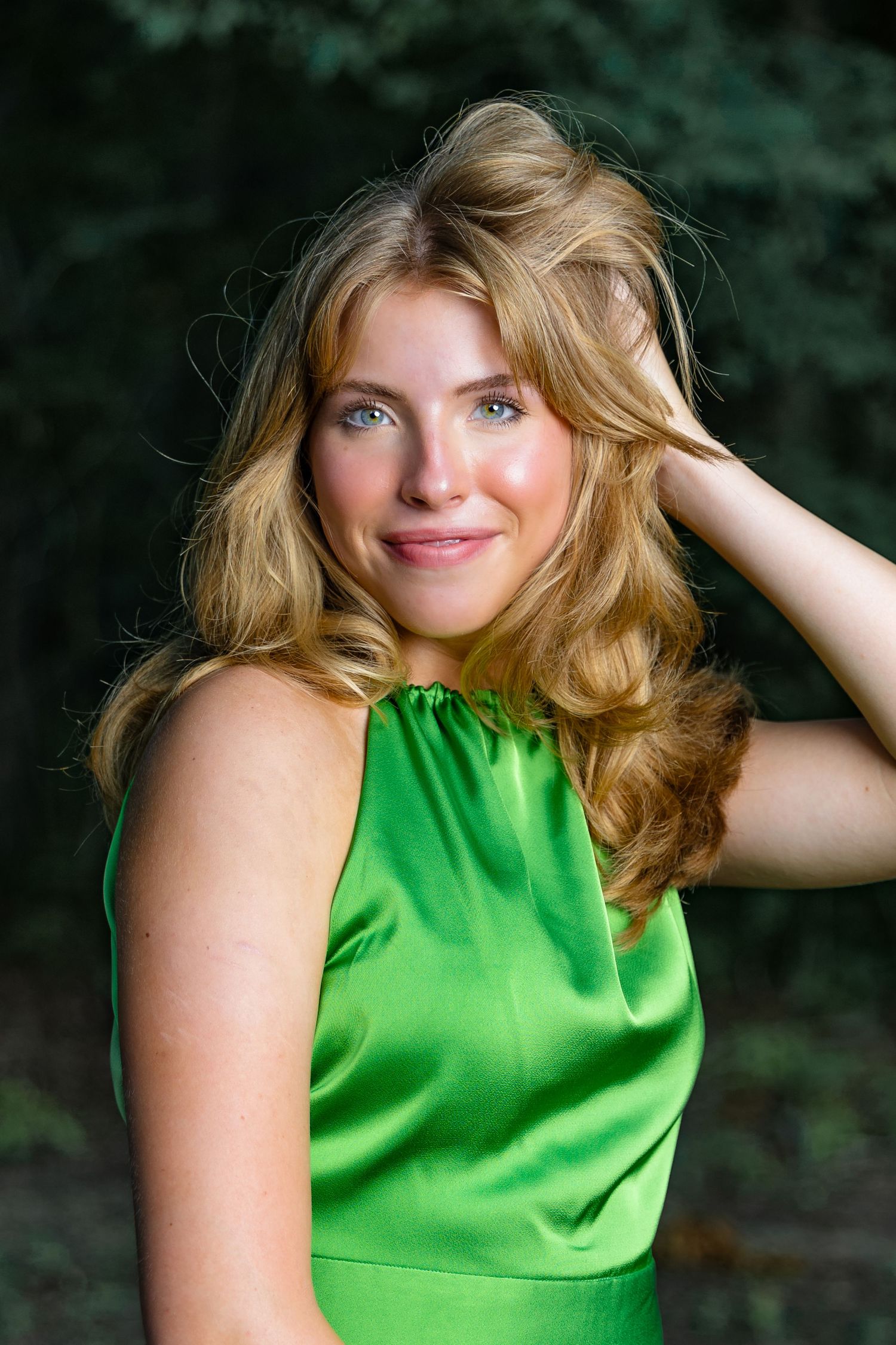 Portrait in a vibrant emerald green satin sleeveless dress against a blurred forest background.