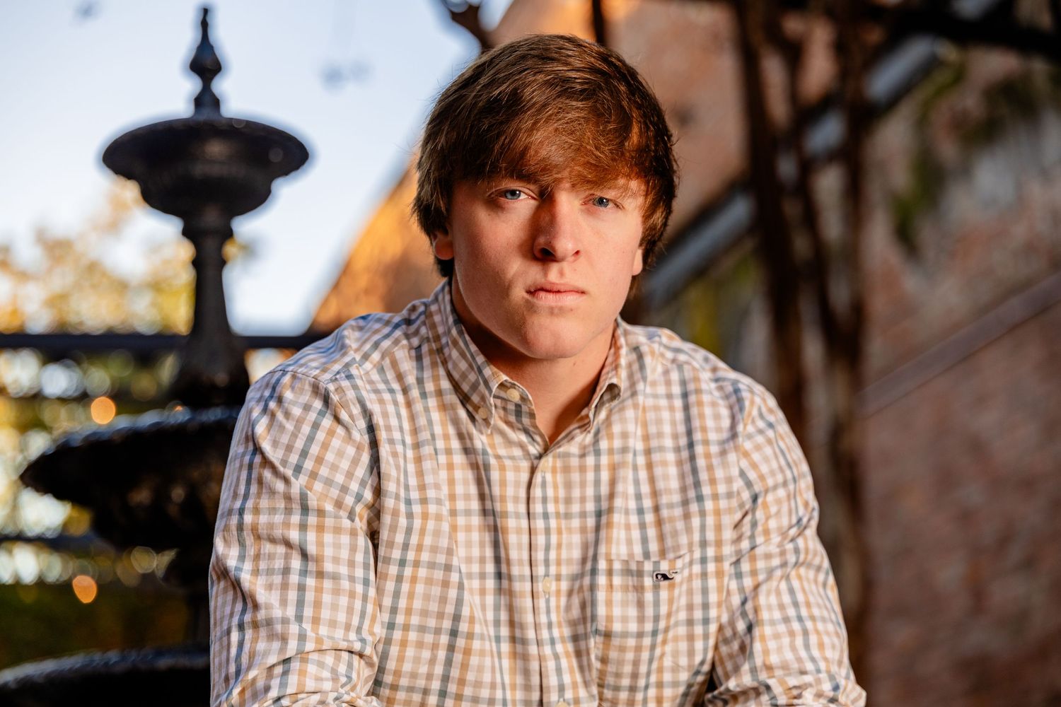 Professional portrait photo taken outdoors with a decorative fountain and warm natural lighting in the background.