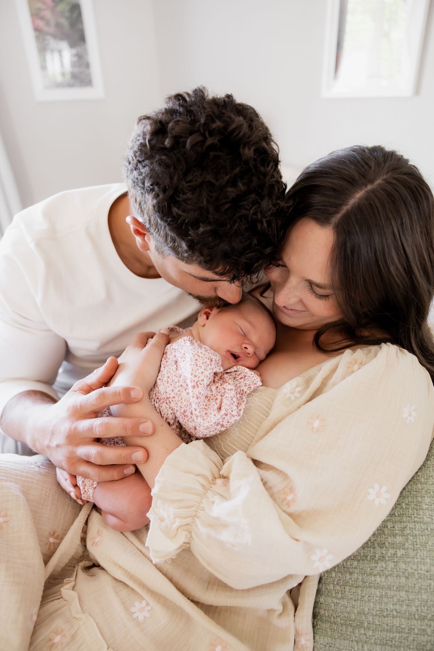 A loving couple cuddles their newborn baby wearing a pink outfit while sitting on a green couch.