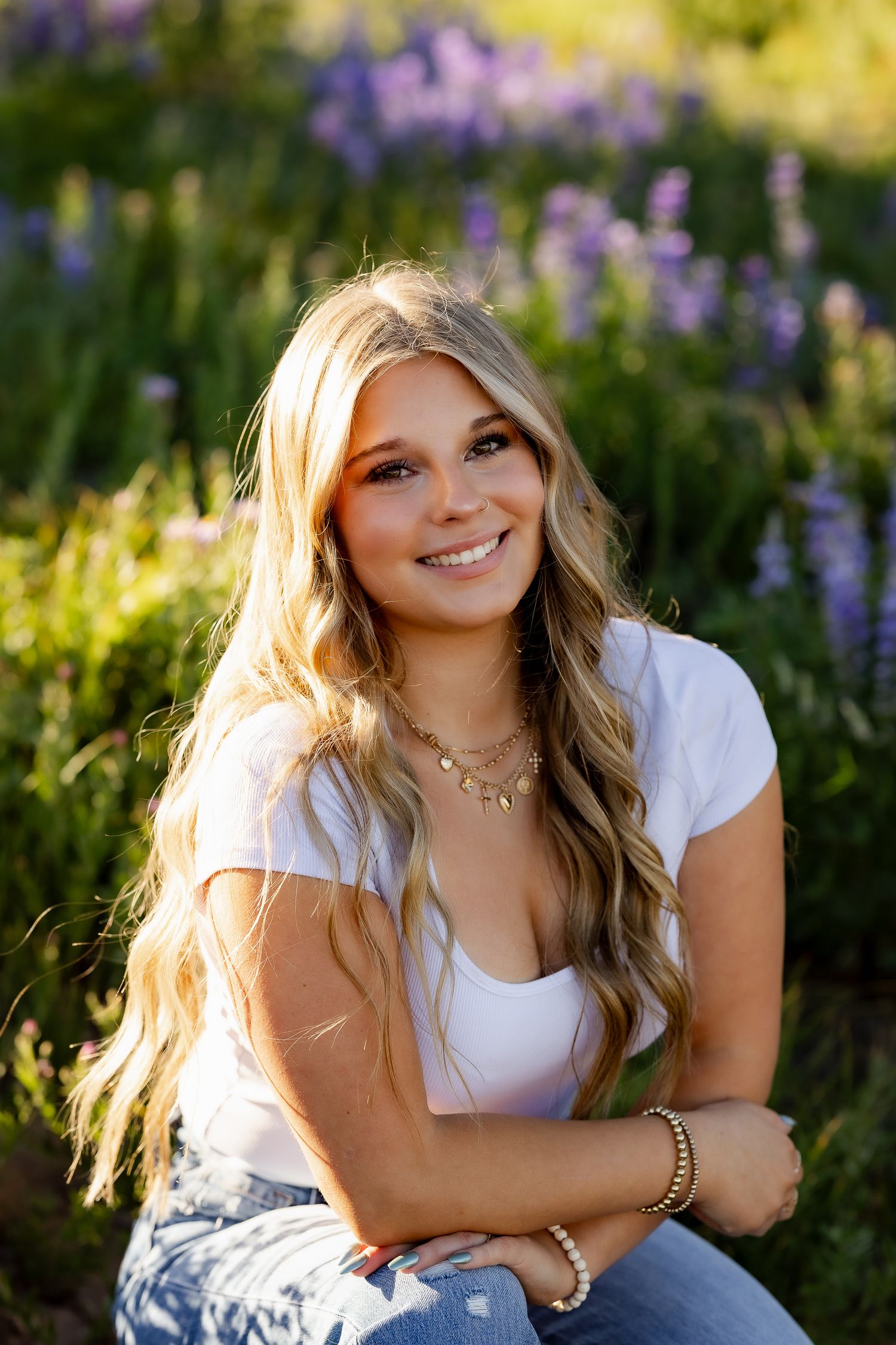 Woman in white top sitting among purple lupine flowers during golden hour.