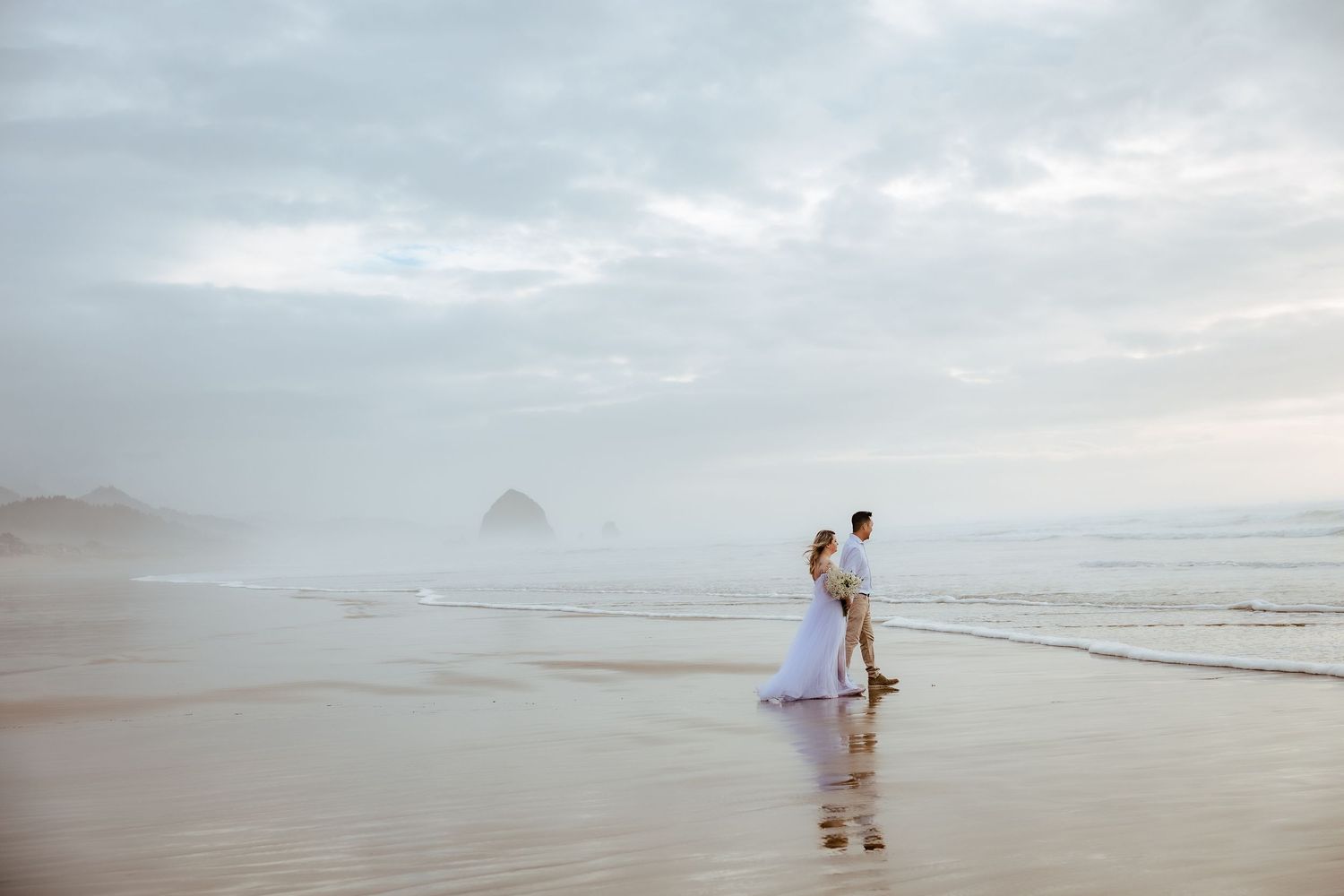 Distant view of couple walking along misty beach shoreline.