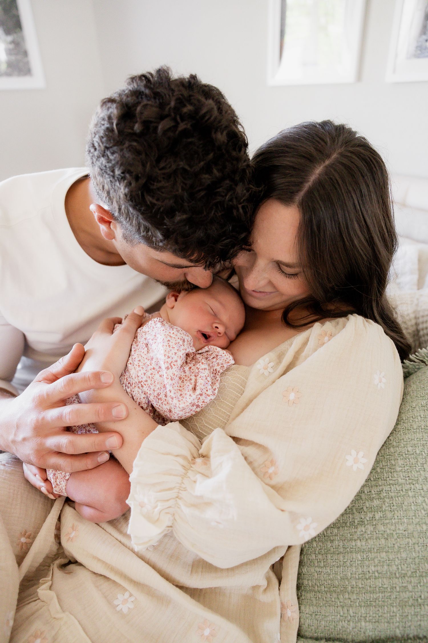 Tender family moment captured on green couch in bright natural light.