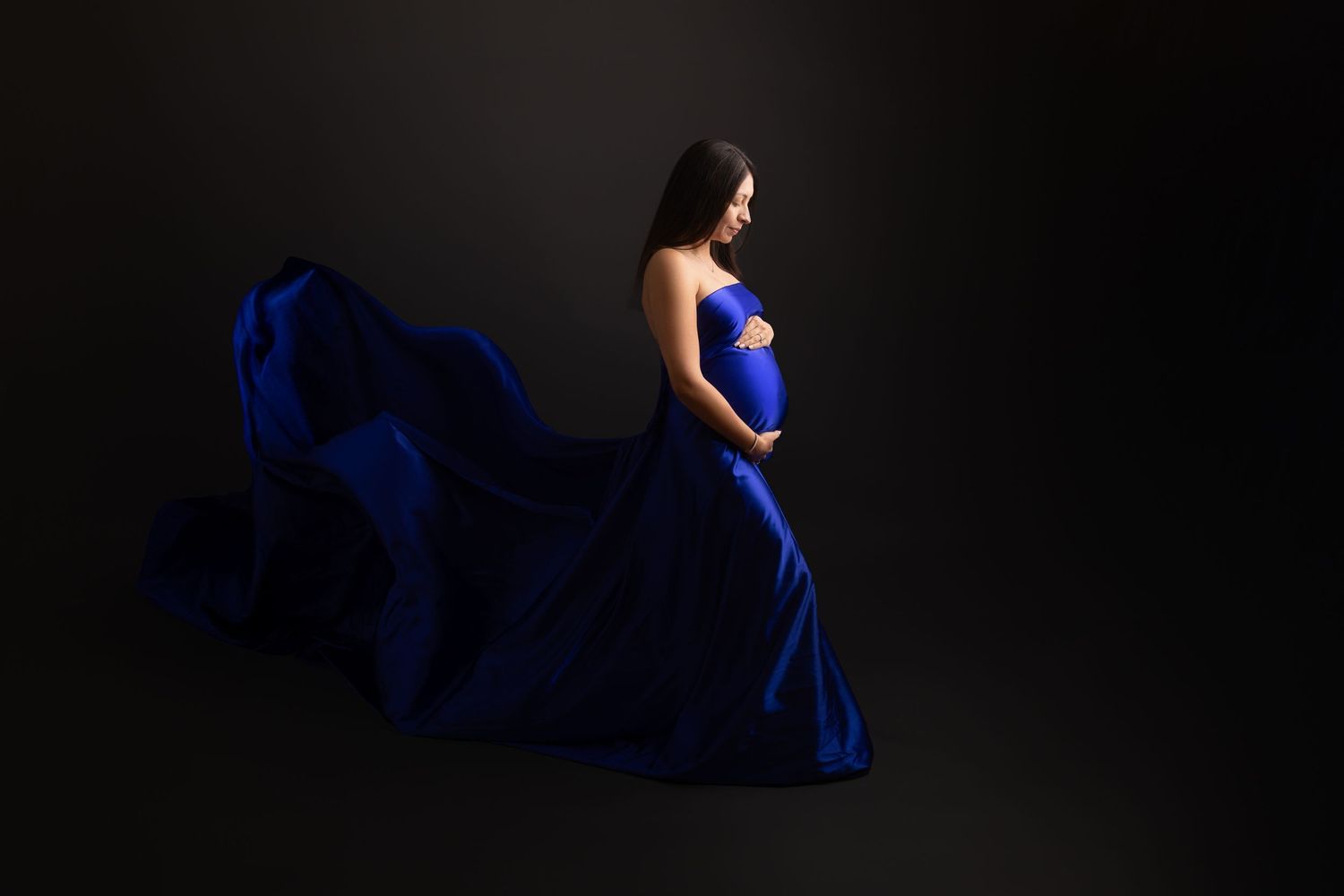A silhouette of a person in a flowing blue dress moves gracefully in a dark studio setting.