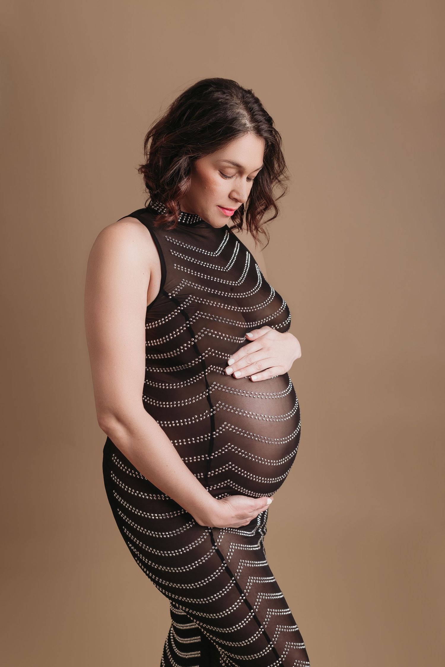 Pregnant woman in a sheer black mesh dress with striped patterns against a nude background for maternity photoshoot in Tampa