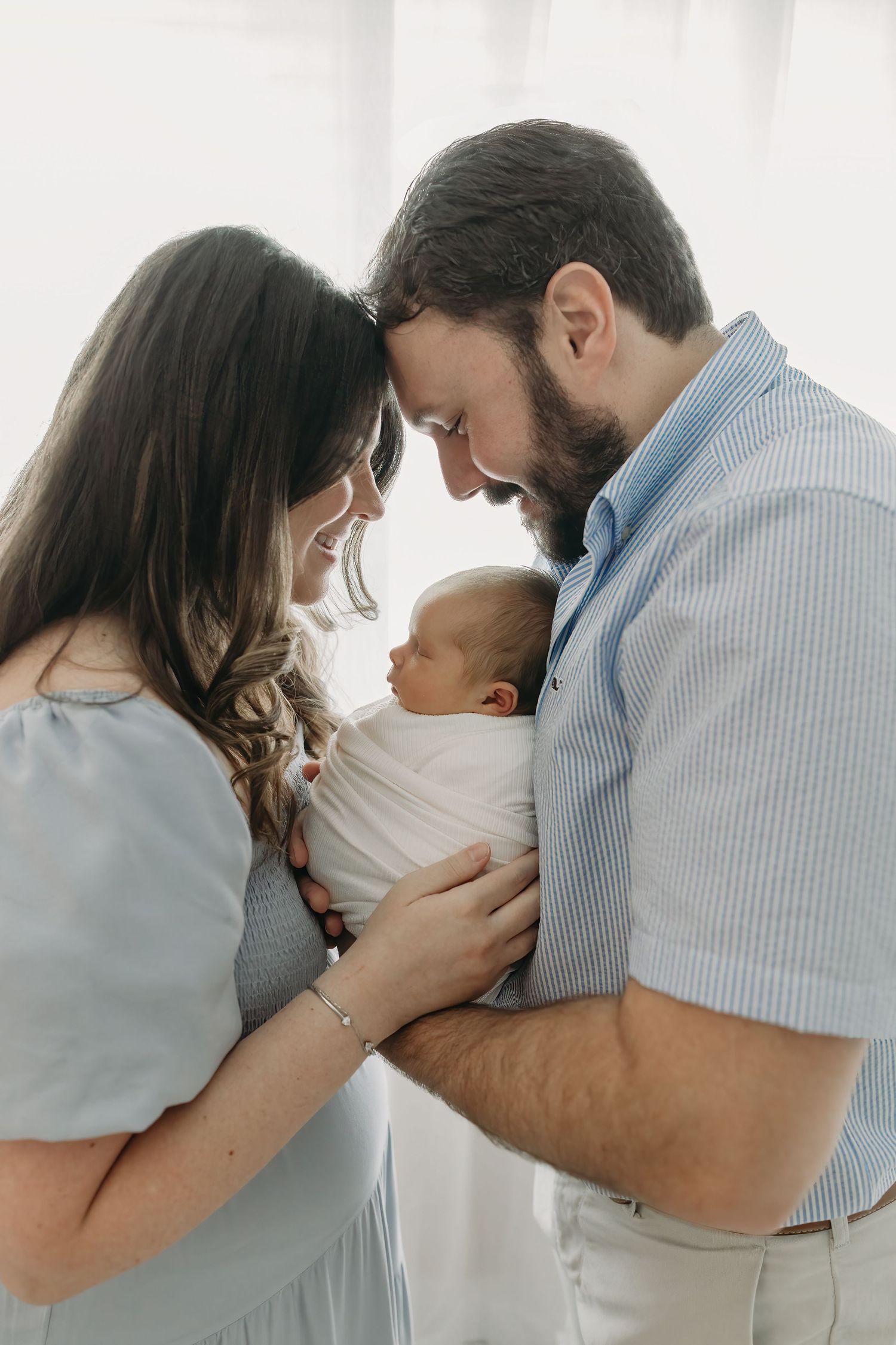 A couple in soft blue and white outfits embrace against a bright, white backdrop in a series of intimate poses.