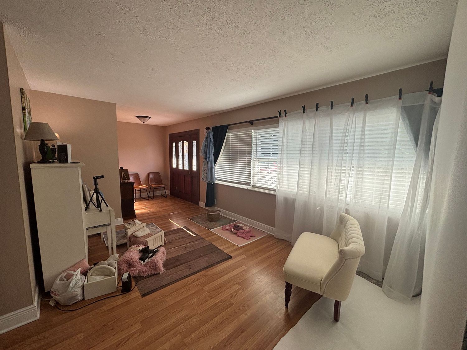 A spacious living room with hardwood floors, sheer curtains, and natural light streaming through large windows.