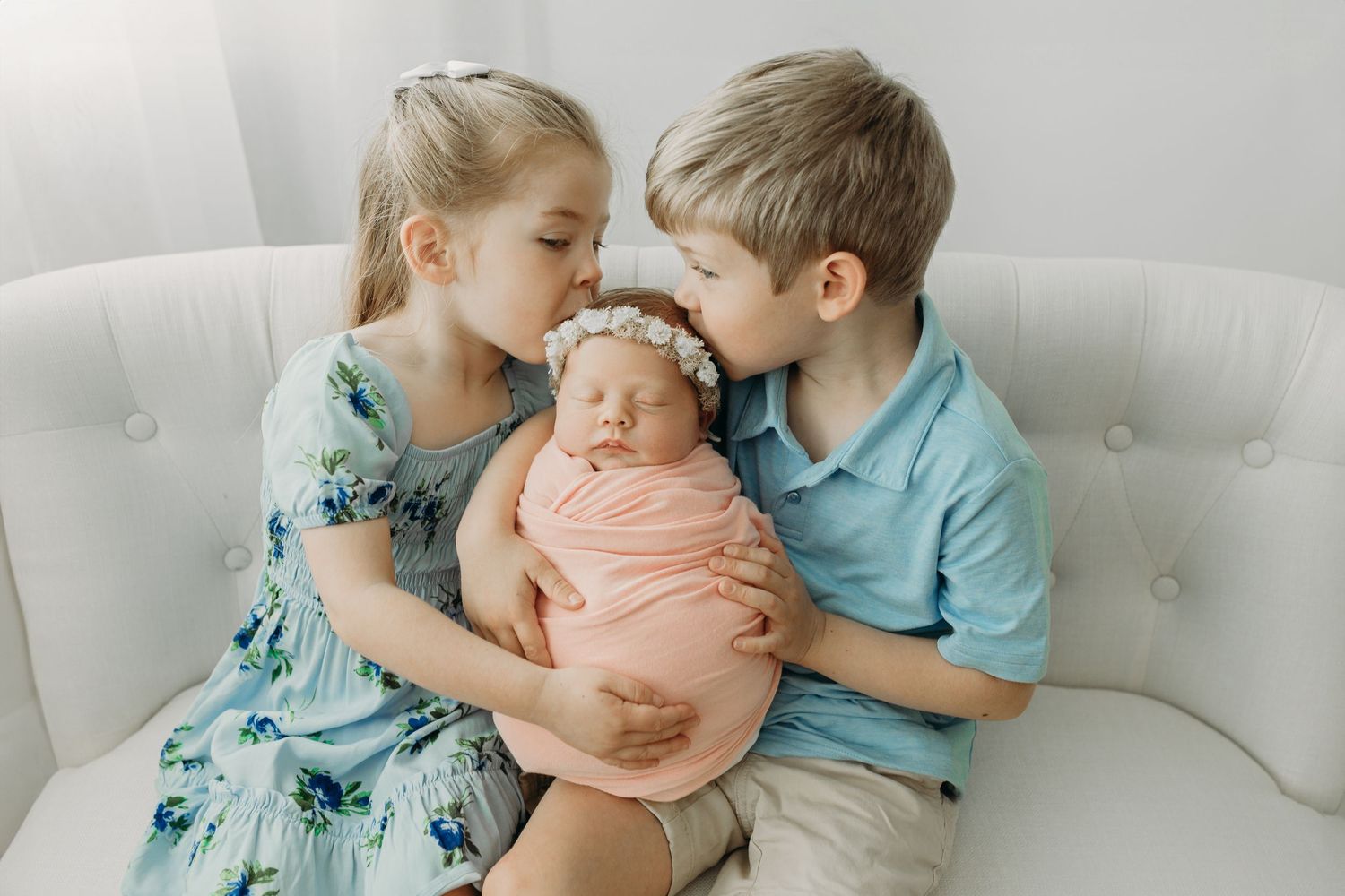 Four connected images show tender moments between siblings with a newborn on a white couch in soft, neutral tones.