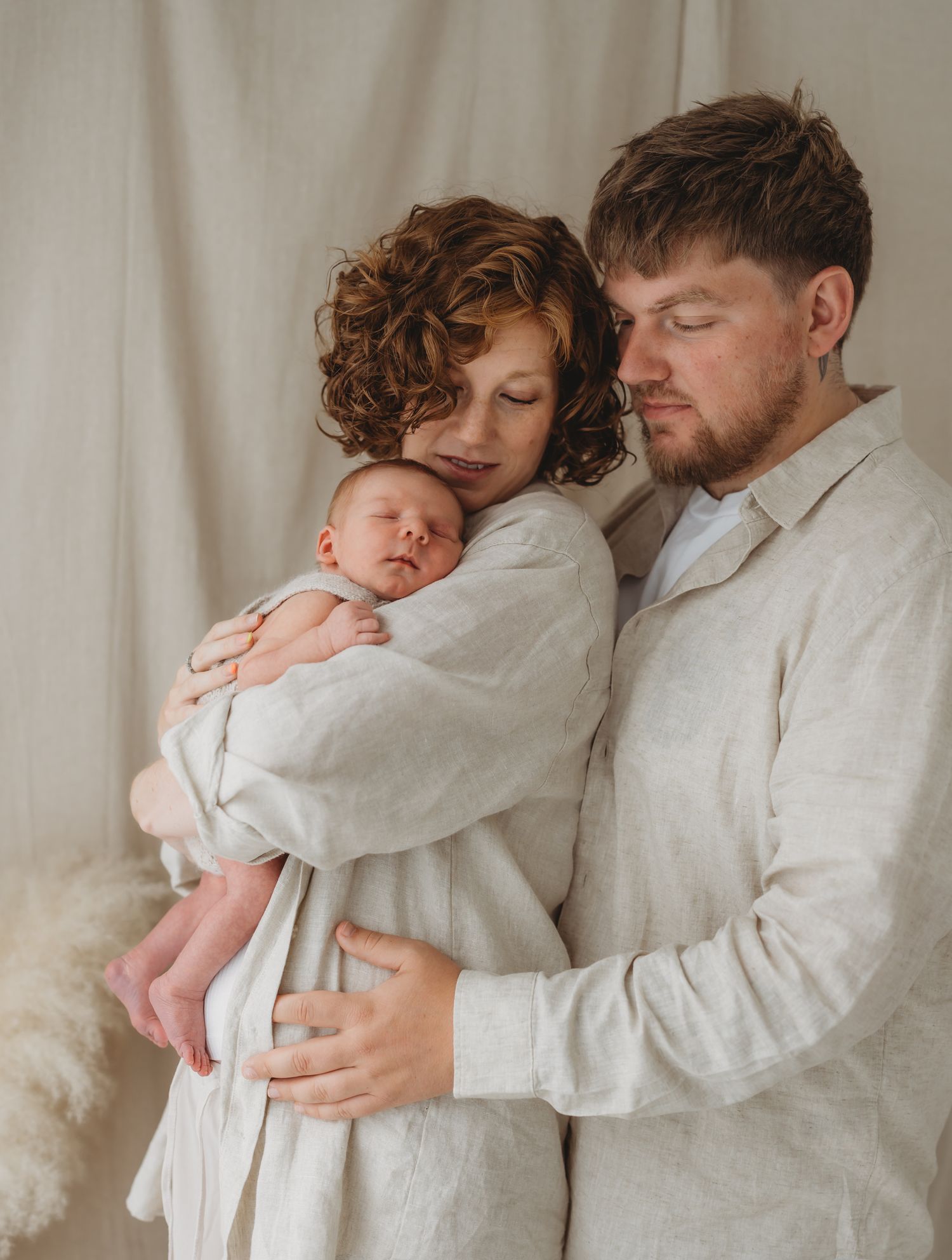 Family in white clothes share an intimate moment while holding their newborn baby, during their family photoshoot in Leicestershire.