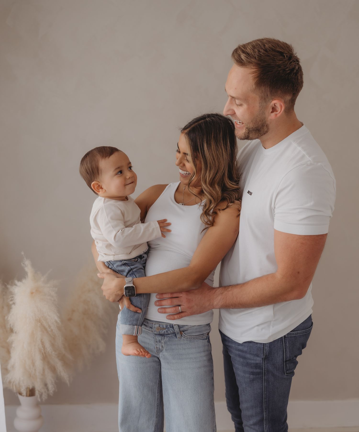 Family in matching white and denim outfits sharing tender moments in a minimalist studio setting.