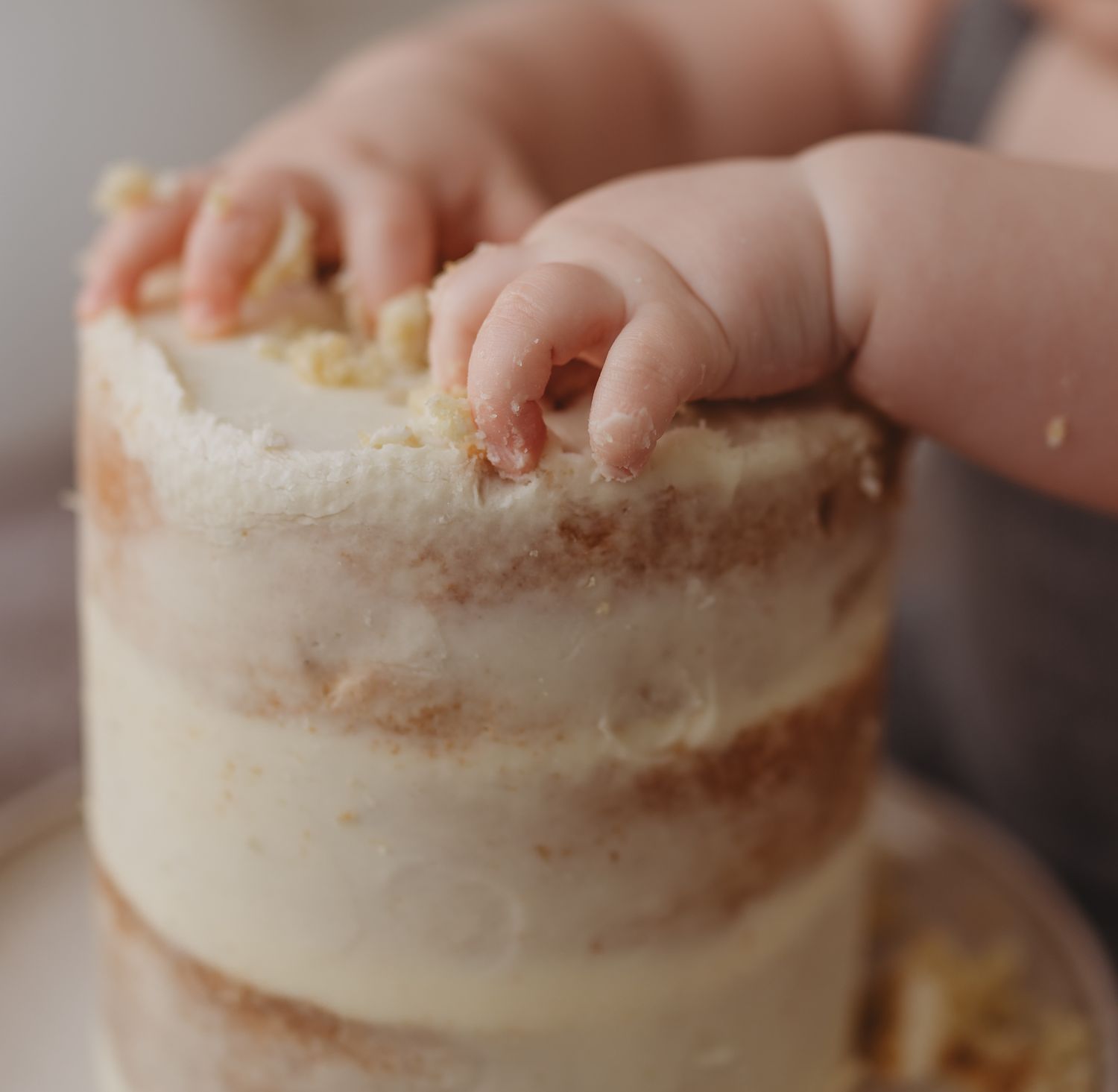 Small hands reach out to touch the top of a white frosted naked layer cake on a cake stand.