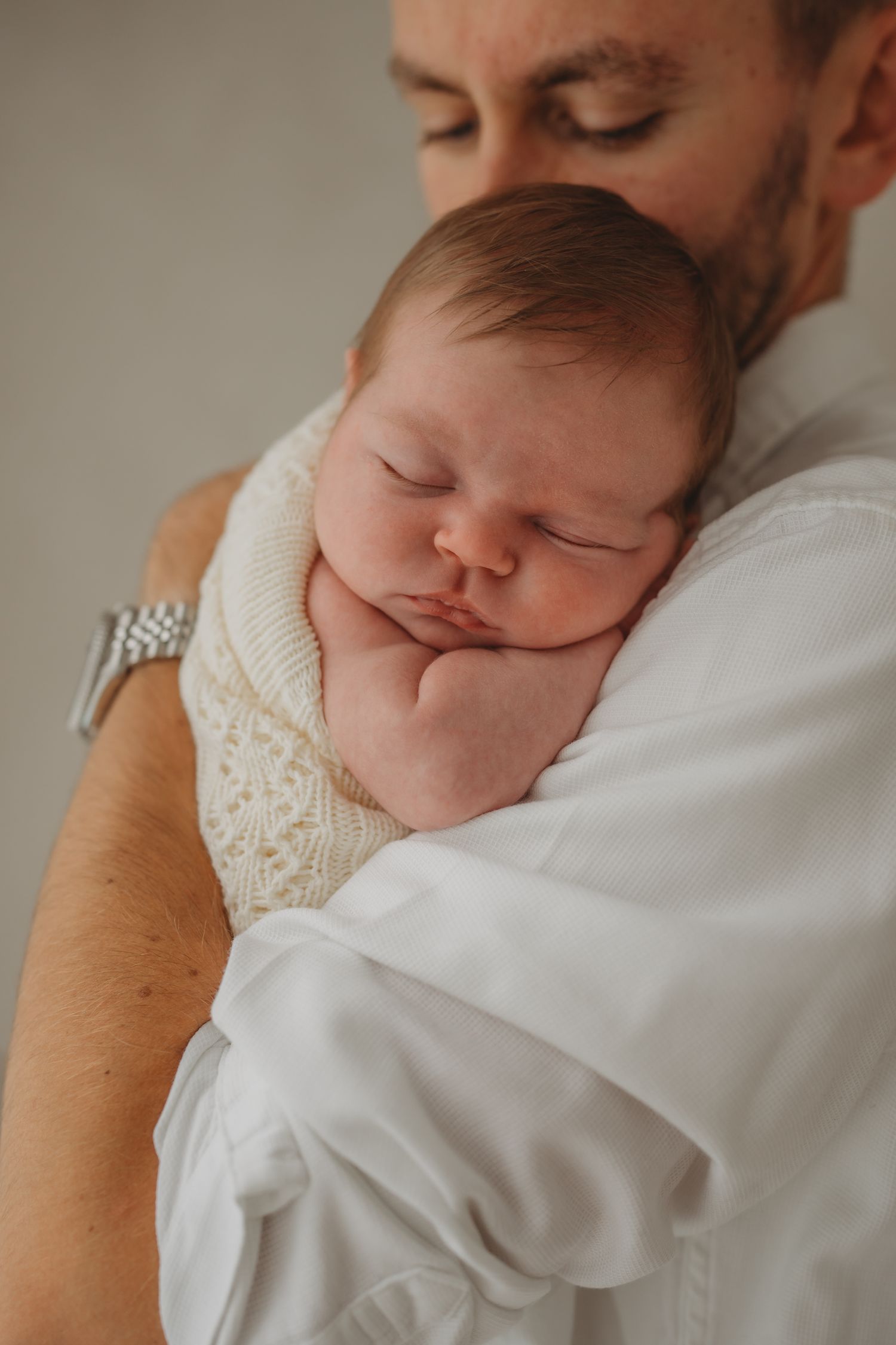 A sleeping newborn baby in white clothing rests peacefully against someone's shoulder.