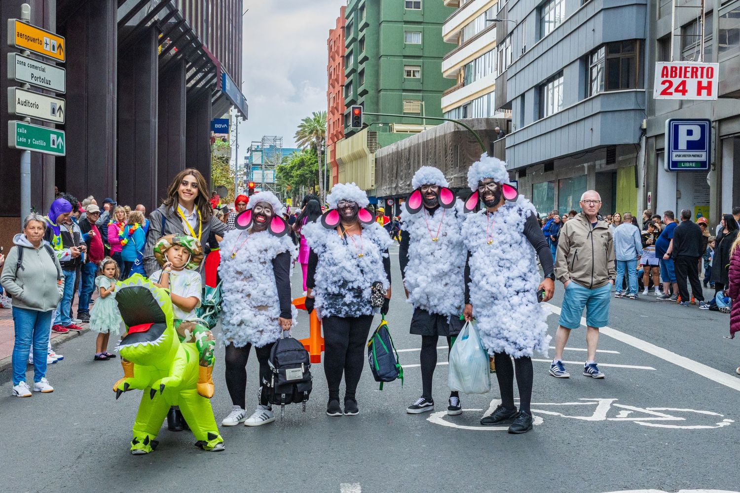 Costumed participants and spectators gather at a street parade with colorful outfits and festive atmosphere in an urban setting.