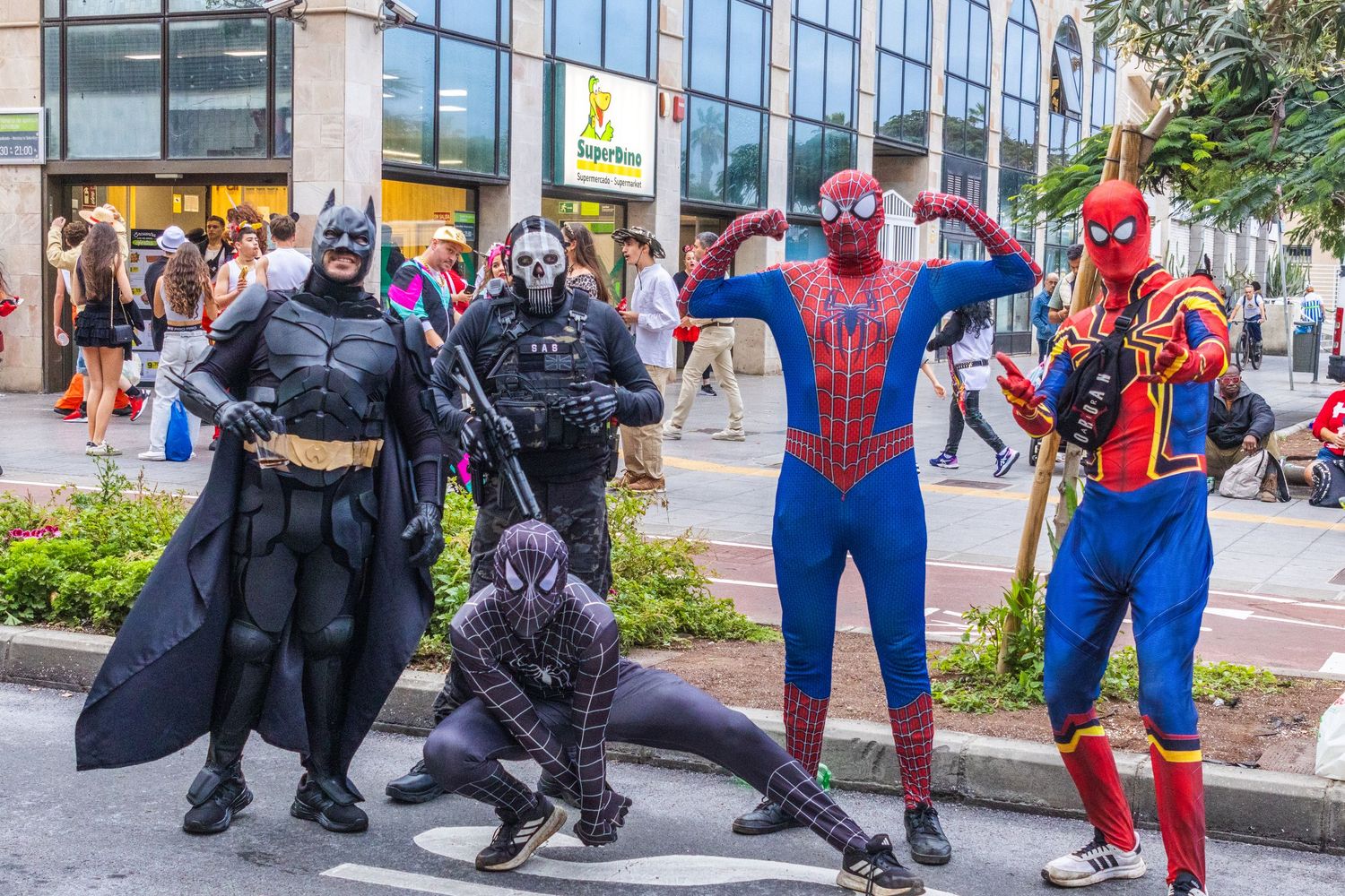 Costumed superheroes pose together on a city sidewalk during a public event.