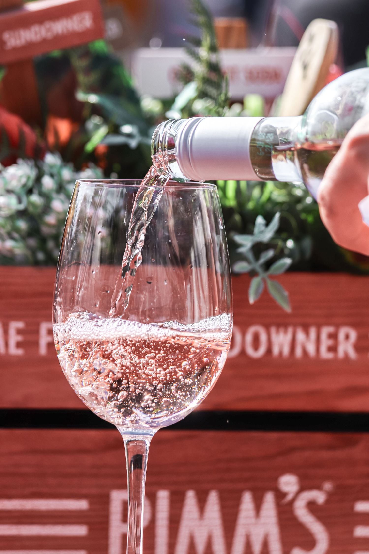 Glasses of sparkling rose wine sit on a table with red decor and greenery in the background.