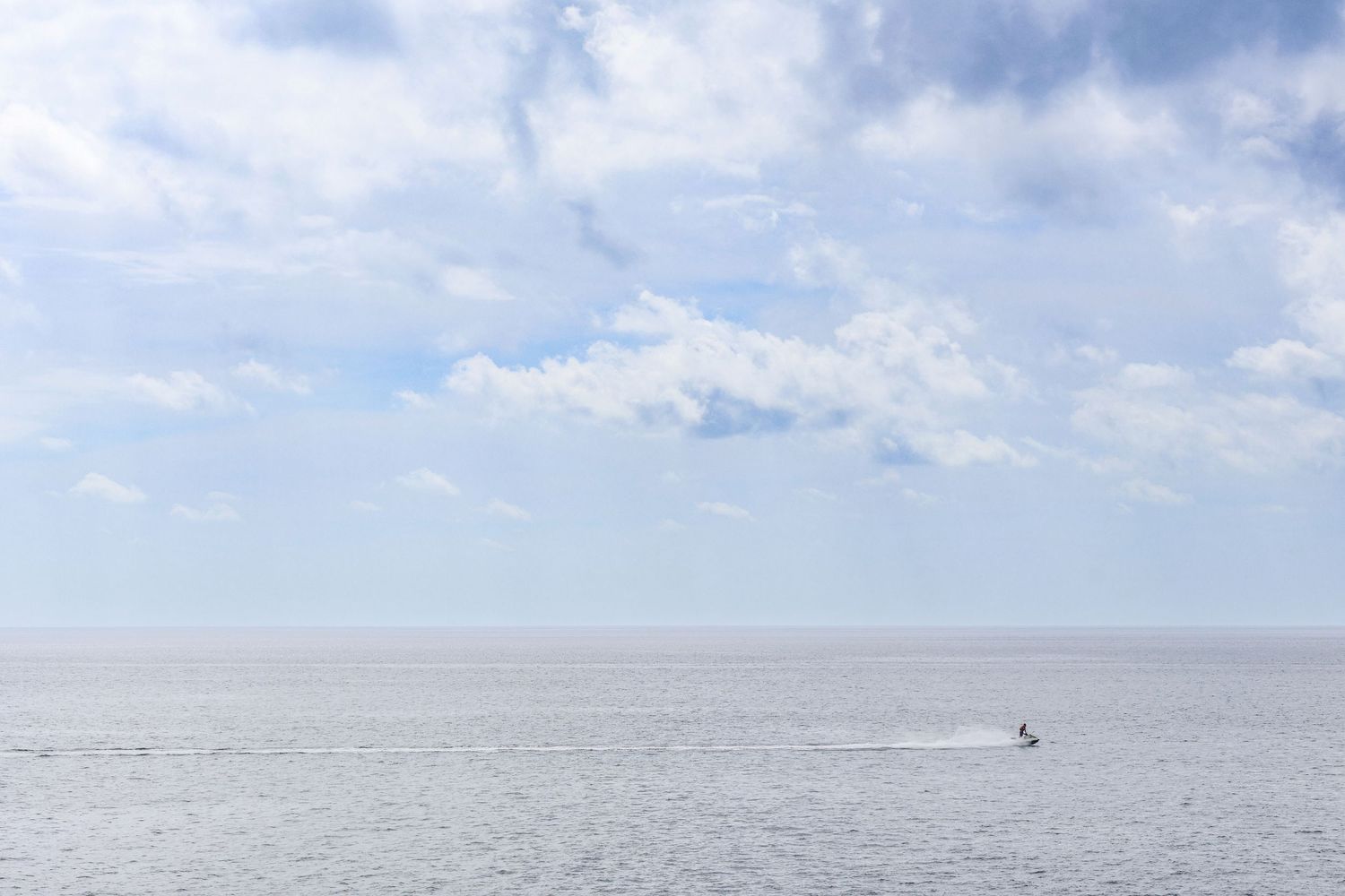 A panoramic view of a vast ocean horizon stretches beneath puffy white clouds in a bright blue sky.