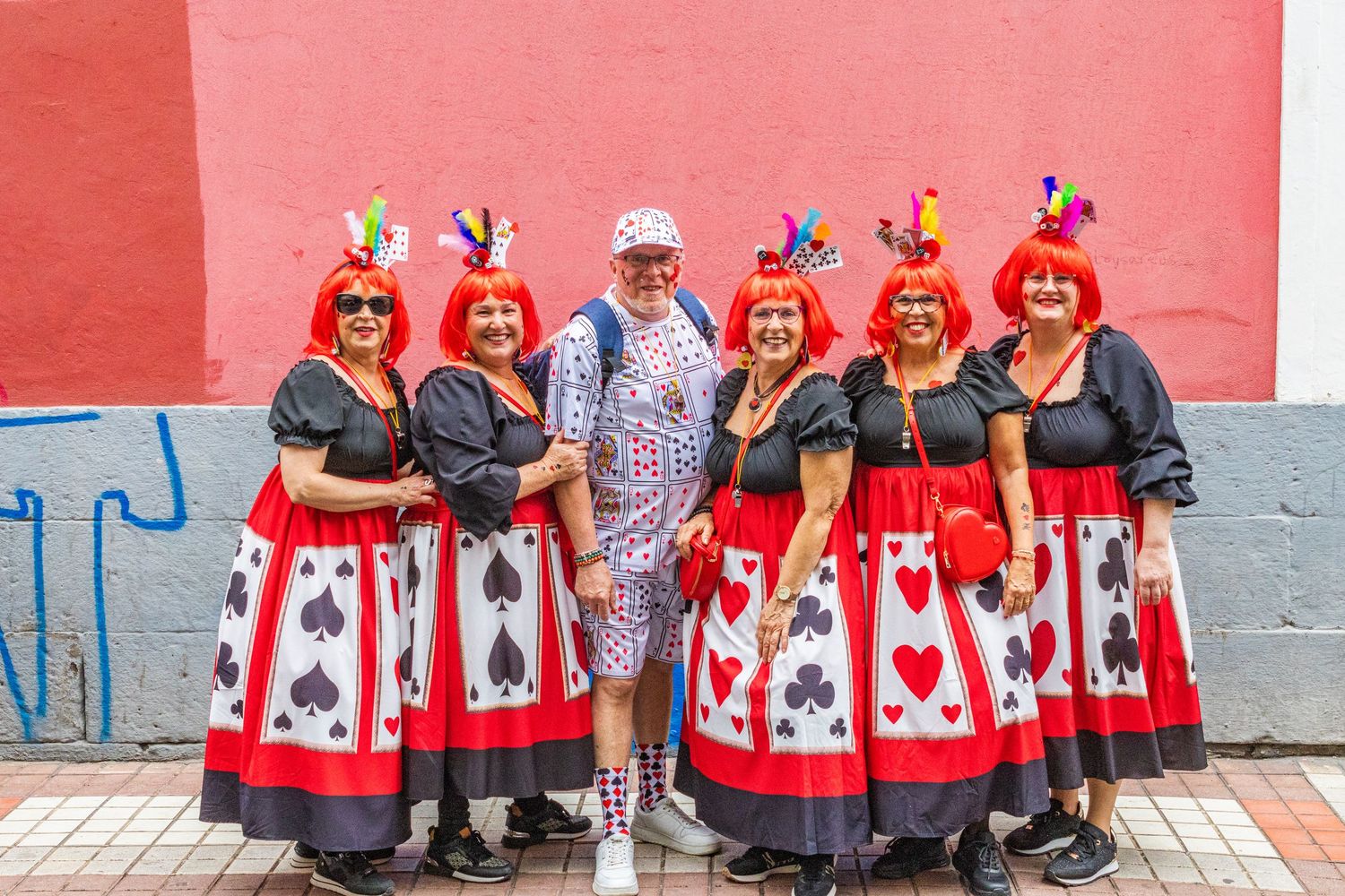 A group of people wearing matching red and white maple leaf aprons stand together against a pink wall.