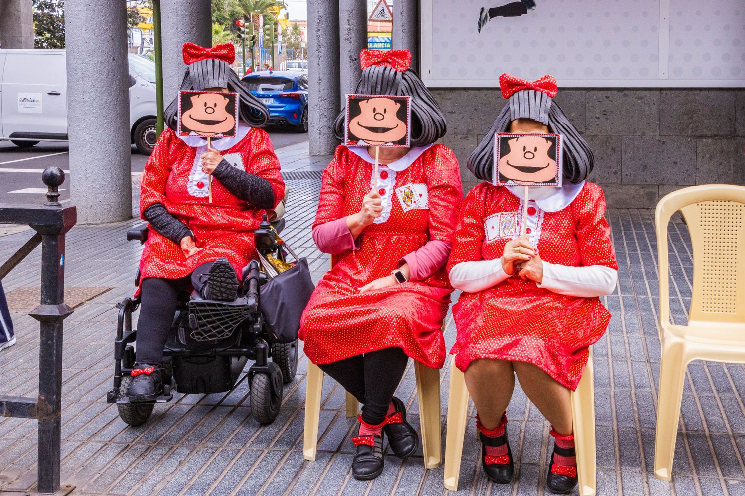 Three delivery workers in bright red jackets sit on plastic chairs outside while taking a break from their duties.