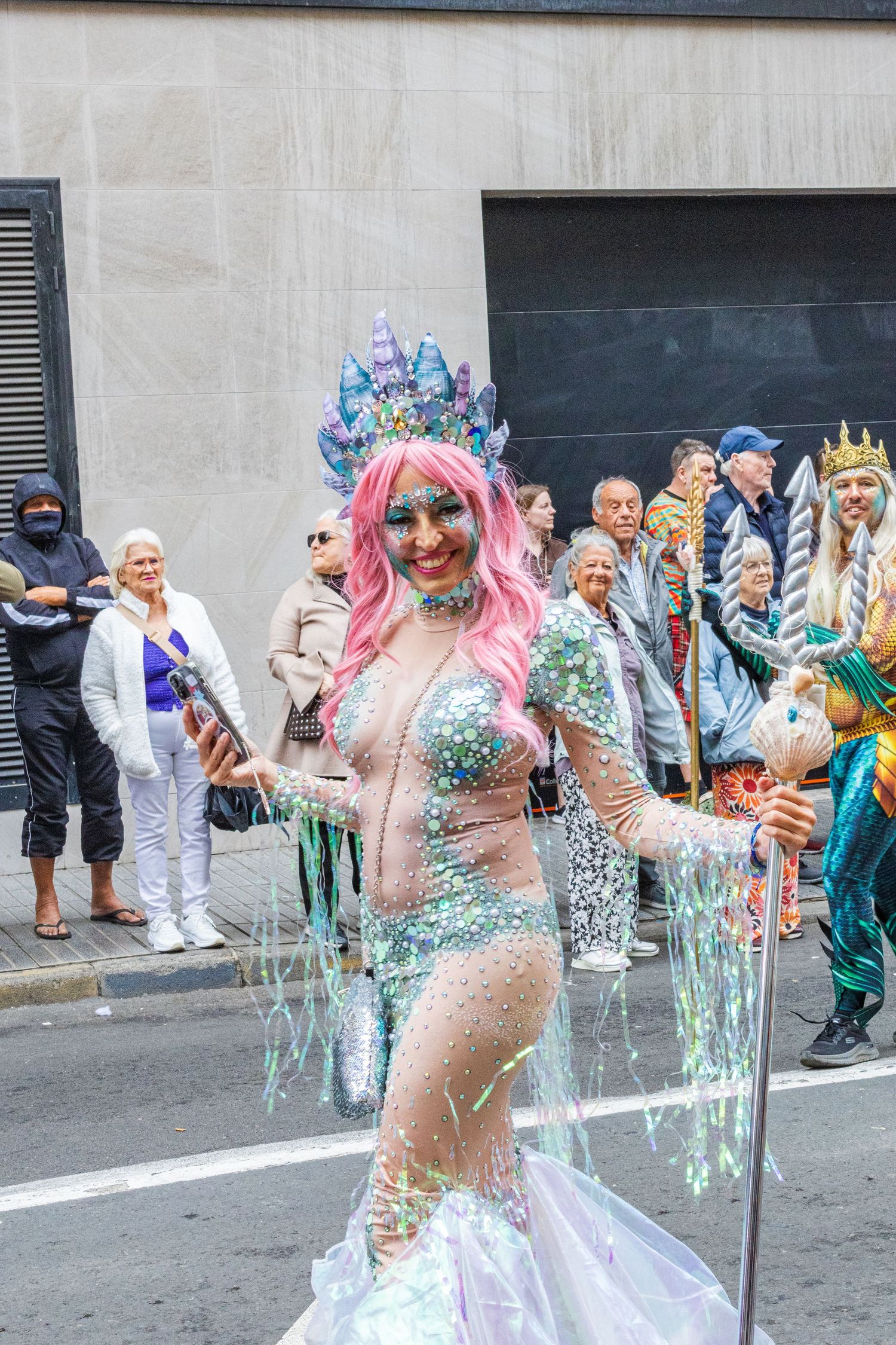 Colorfully dressed performers in glittery costumes parade down a street during a festival celebration.