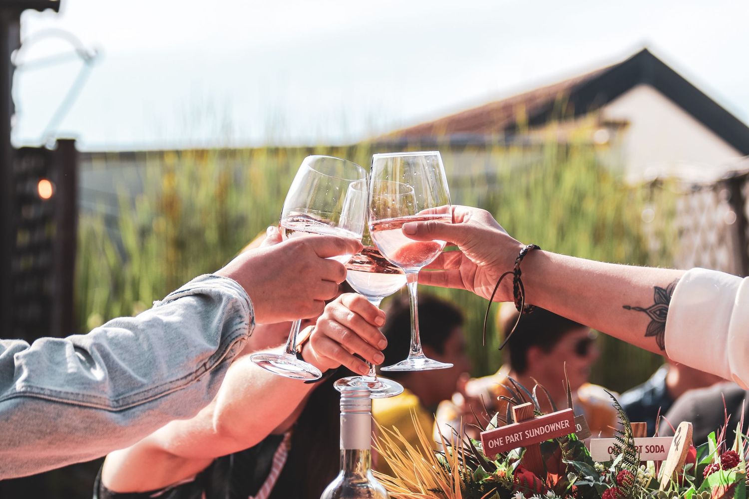 Wine glasses clink together in a toast during an outdoor dining experience at sunset.