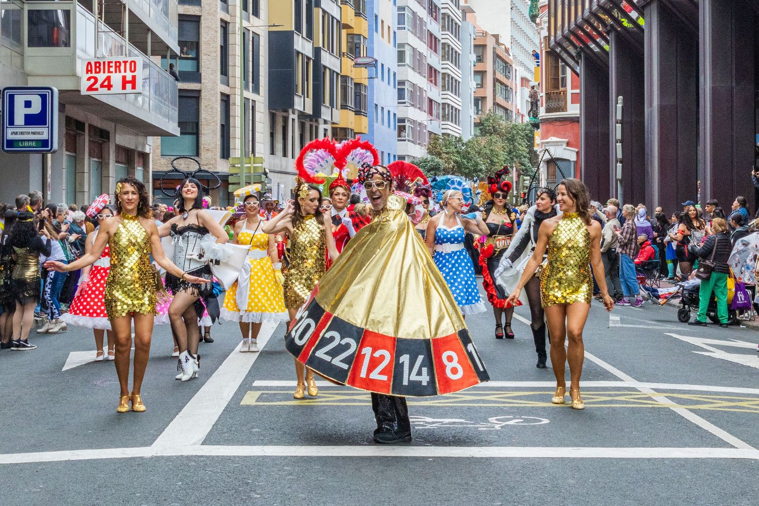 Colorful parade performers in gold and yellow costumes dance down a city street during a festive celebration.