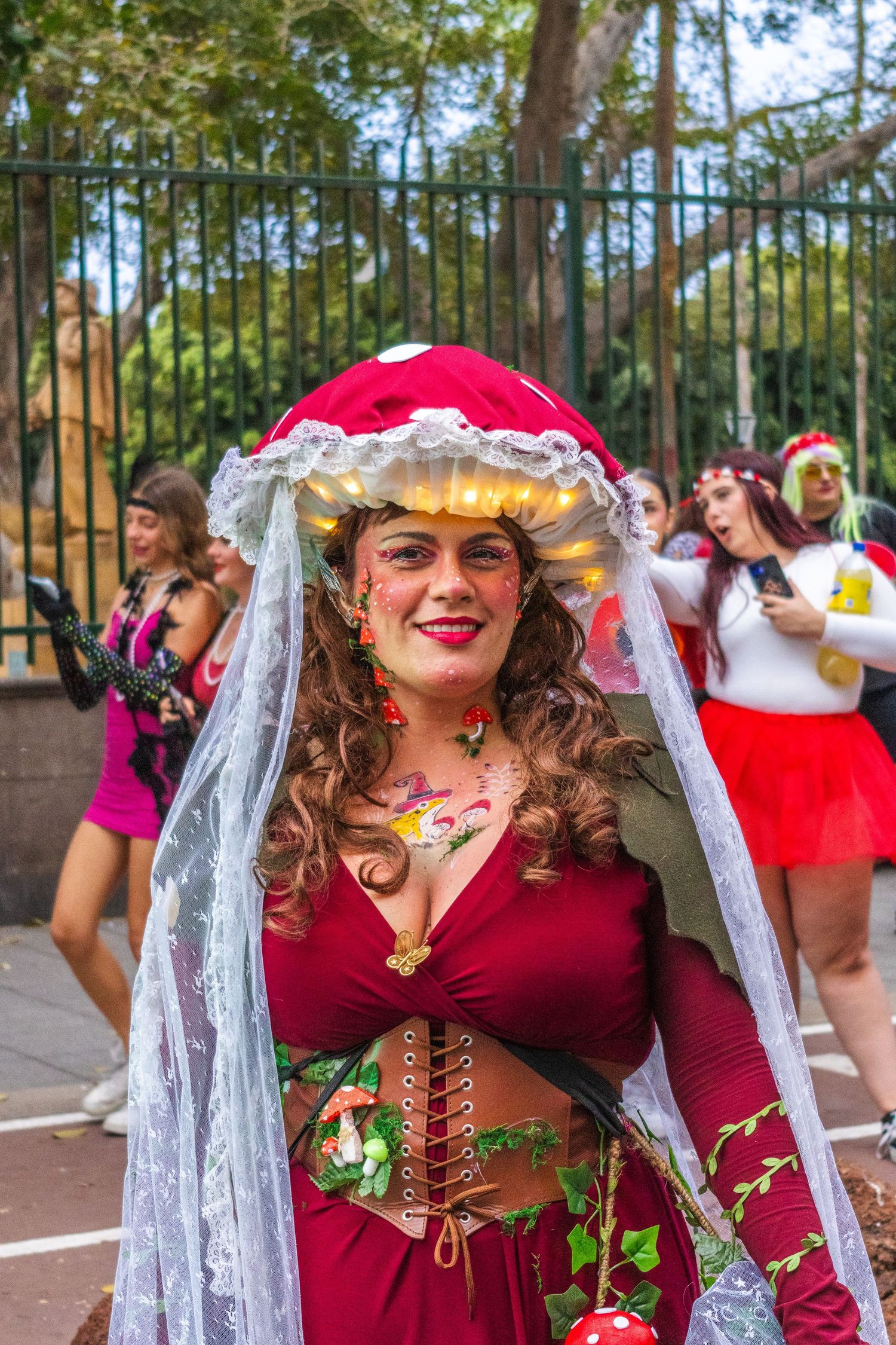 A group of performers in medieval renaissance fair costumes with red dresses and lace veils dance outdoors.