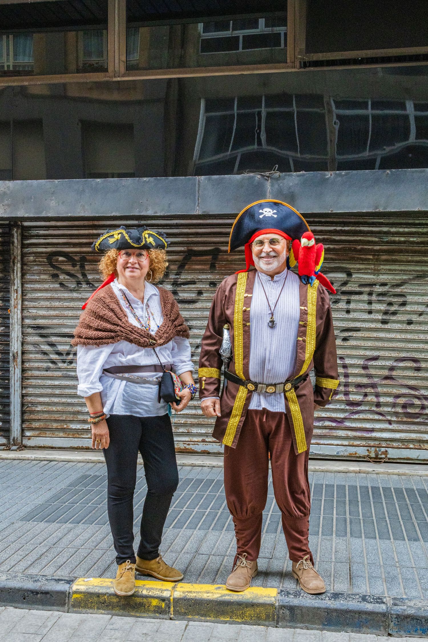 Two people in traditional medieval costumes pose together on a sidewalk in front of a building.