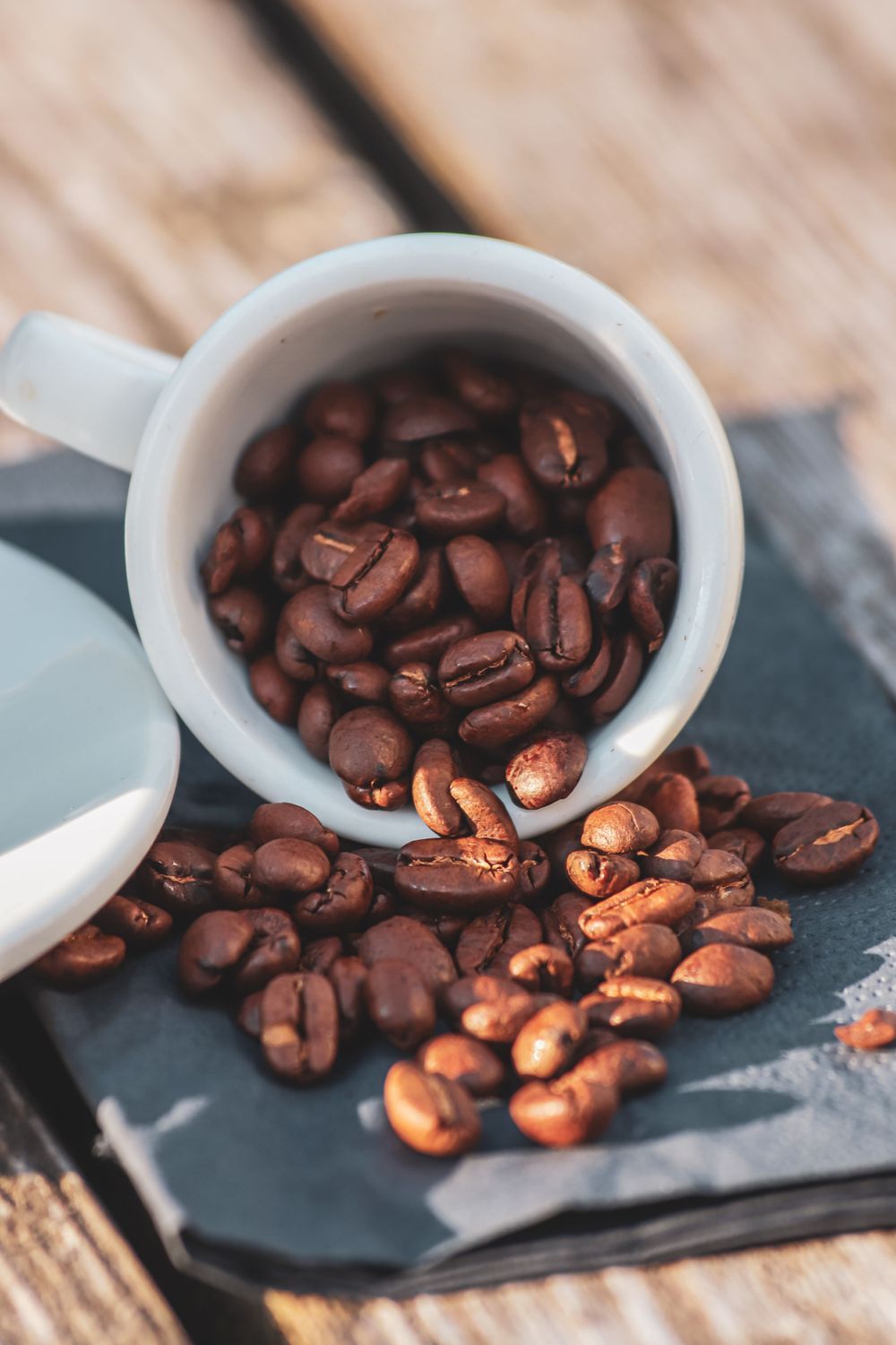 Fresh roasted coffee beans spilling from a white ceramic bowl onto a dark surface.