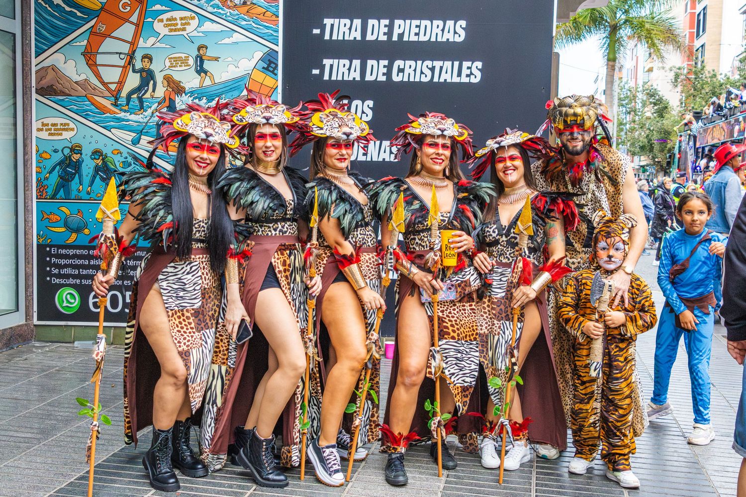 Colorful carnival performers in elaborate feathered costumes and headdresses dance during a street parade celebration.