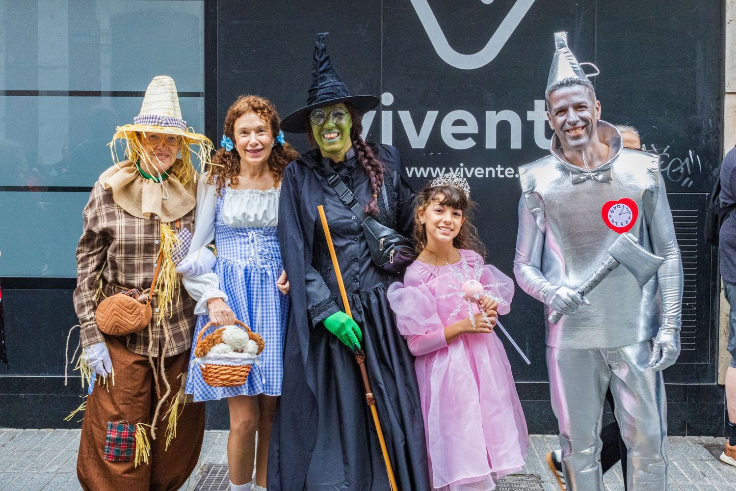 Four people dressed as characters from The Wizard of Oz pose together in front of a storefront window.