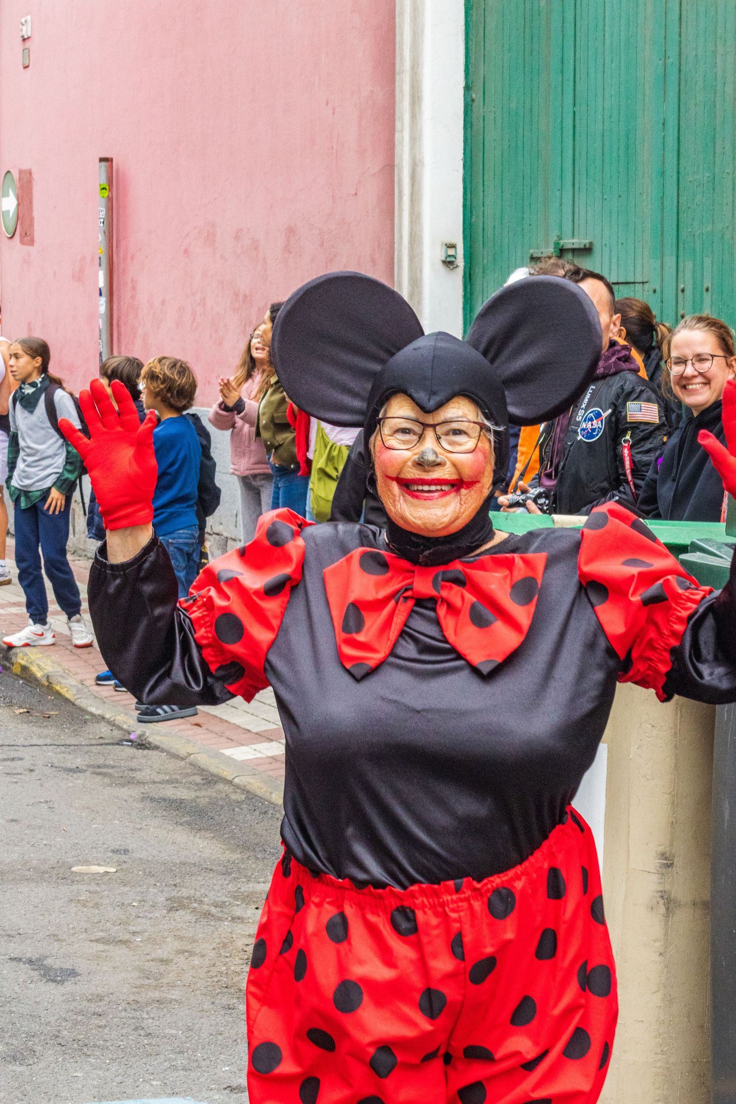 Three images show someone in a ladybug costume with black polka dots and red ruffles dancing and posing against a pink wall.