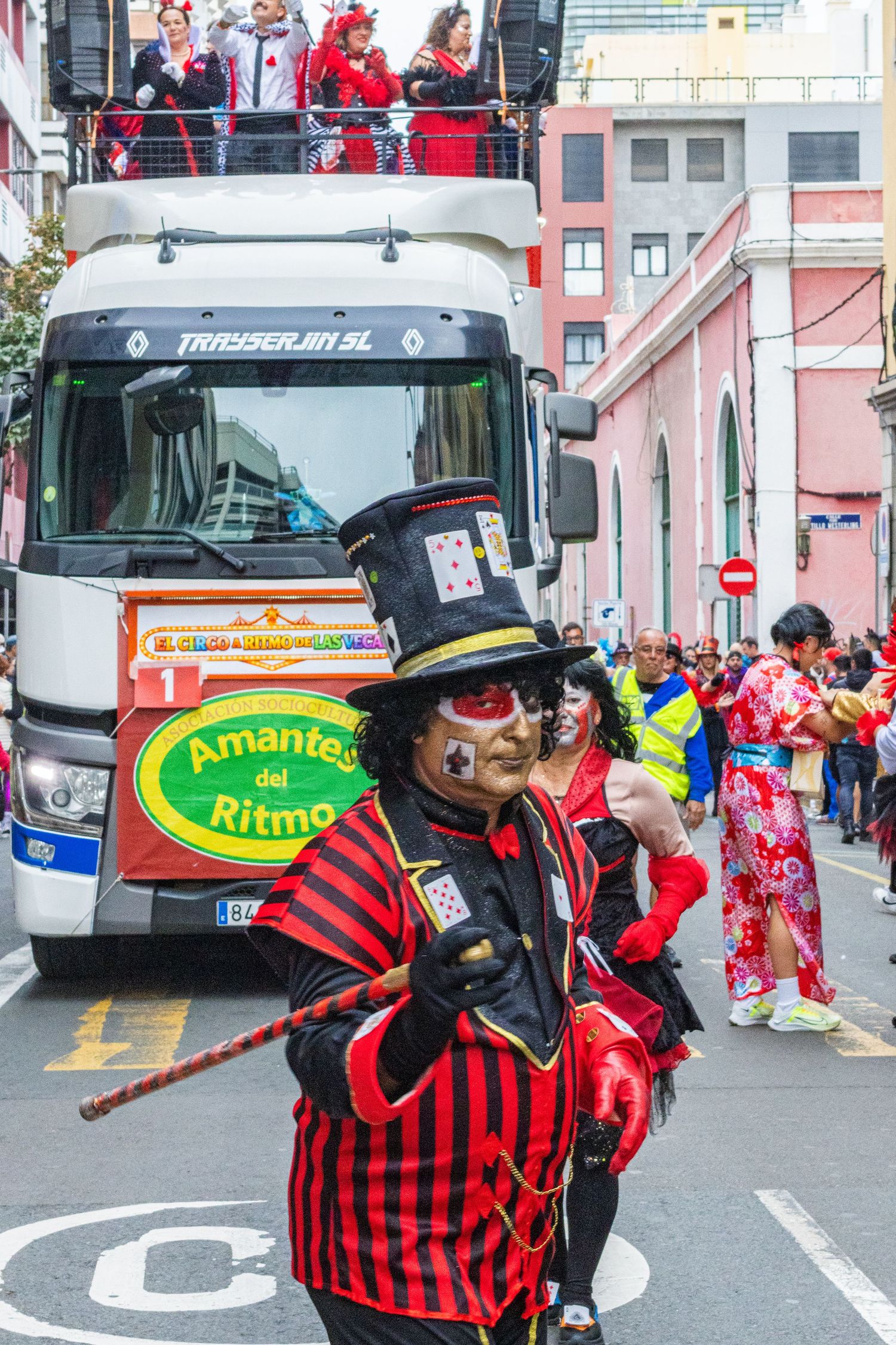 Performers in red and black striped costumes and masks entertain during a street festival near parked buses.