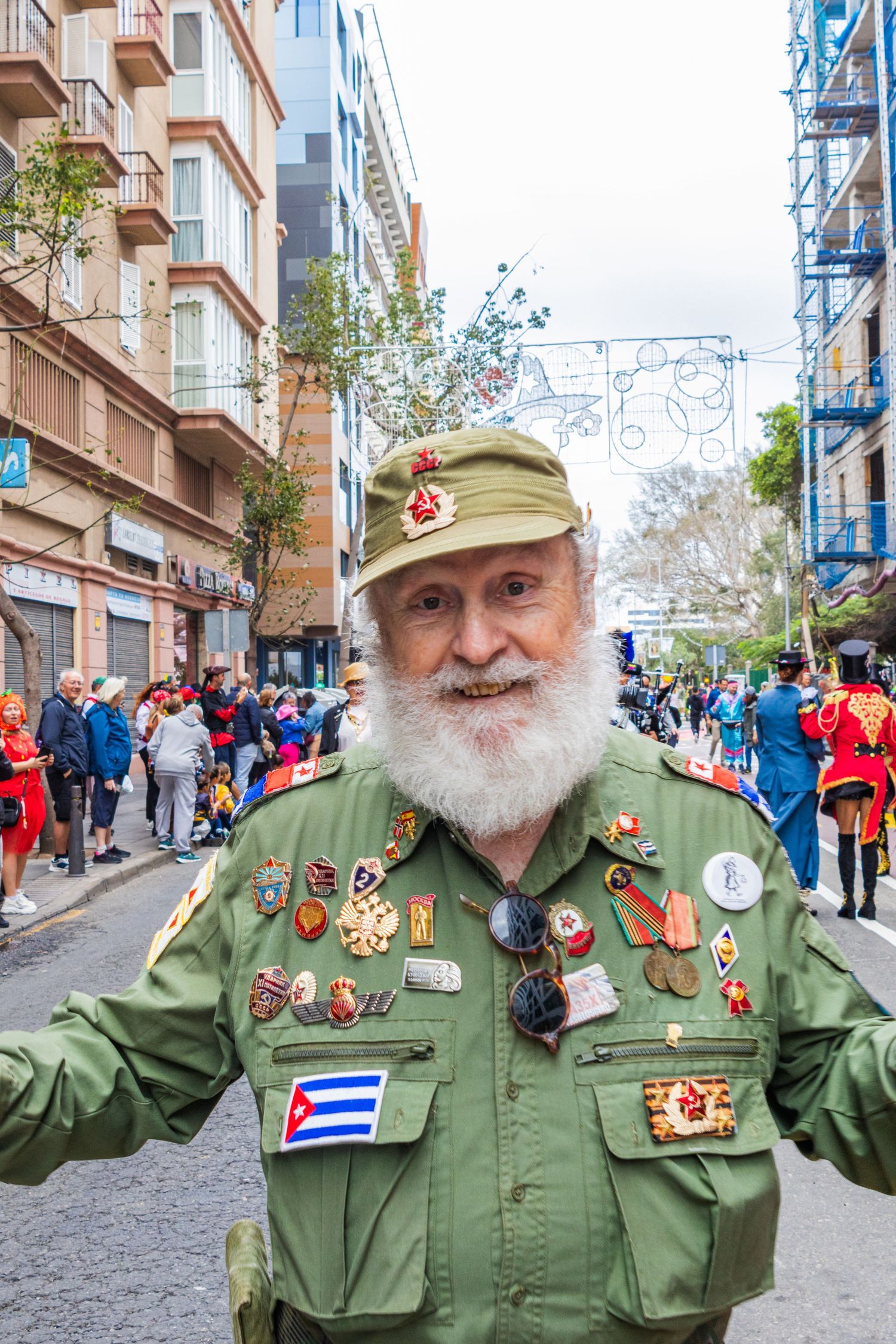 Military veteran wearing olive green uniform with Cuban flag patch and numerous medals on a crowded city street.