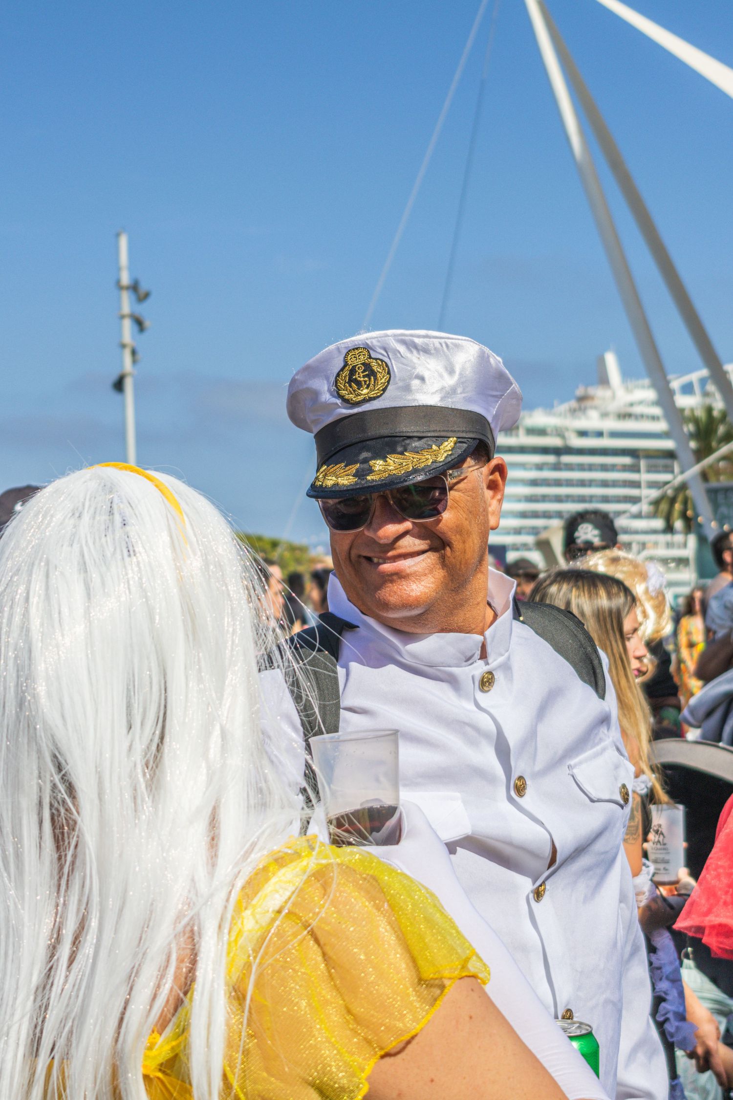 A group of people in naval uniforms and costumes gather at an outdoor event on a sunny day with palm trees visible.