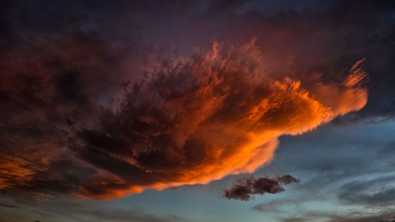 Fiery red and orange clouds at sunset against a dark dramatic sky.