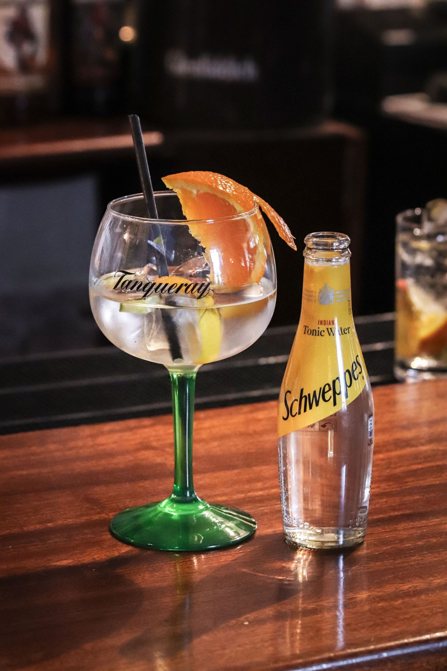 Cocktail glasses and bottles arranged on a dark wooden bar counter with a Schweppes bottle visible in the background.