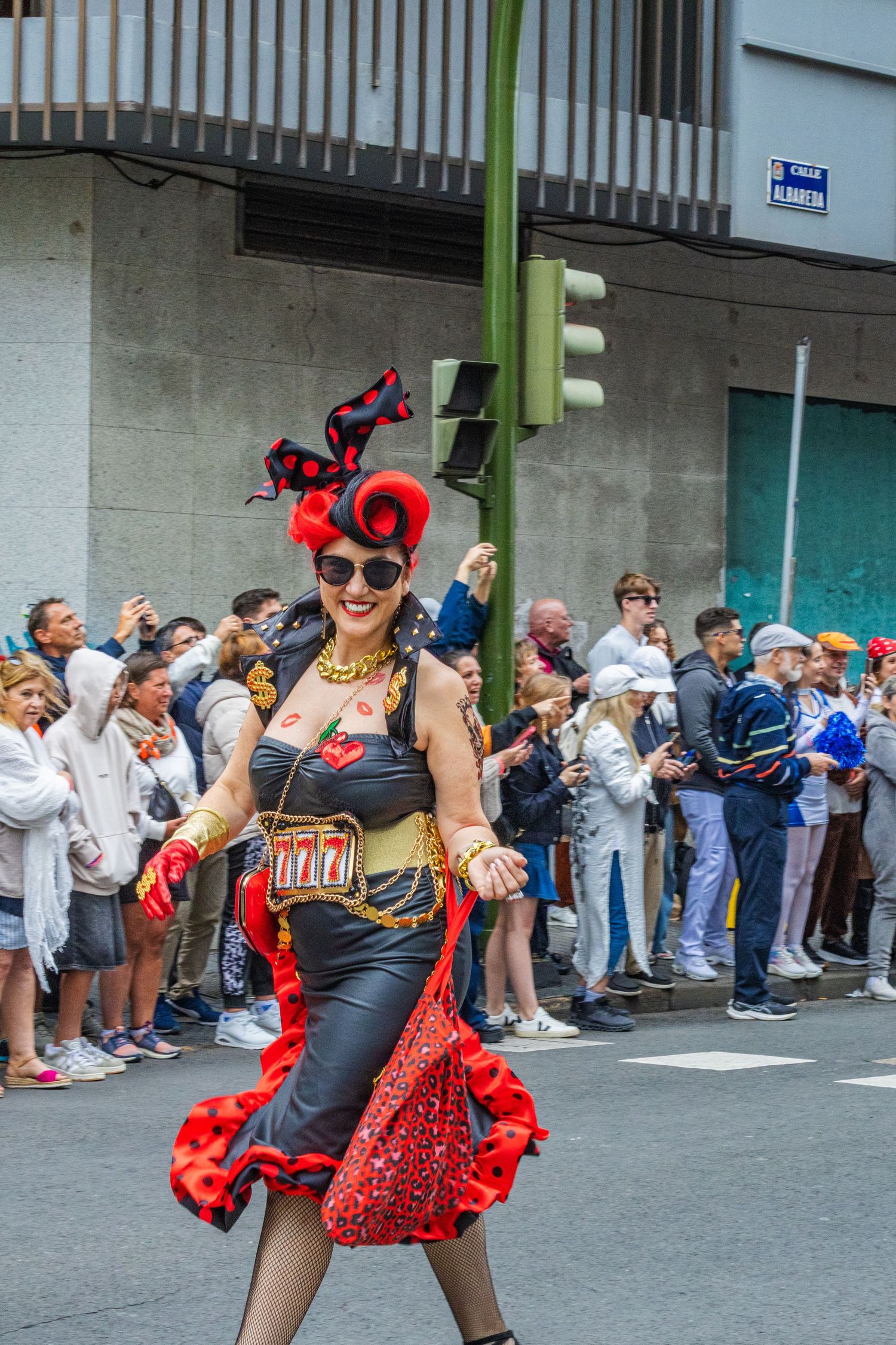 Street performers in black and red dance costumes entertain a crowd of spectators lined up along a building wall.