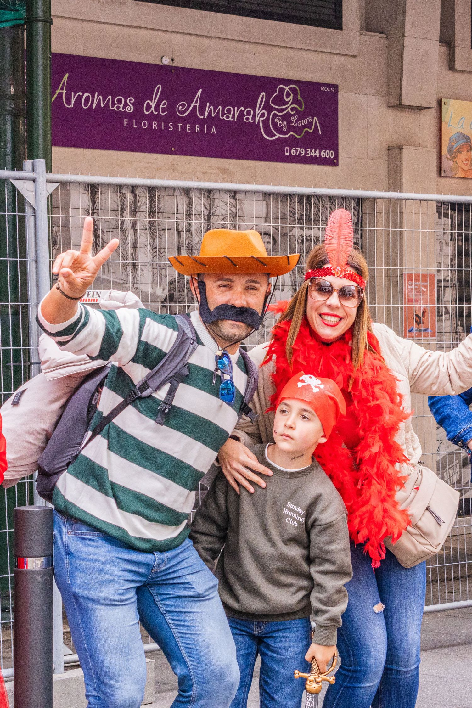 Group of friends in striped shirts and costumes pose playfully on a city sidewalk outside a storefront.