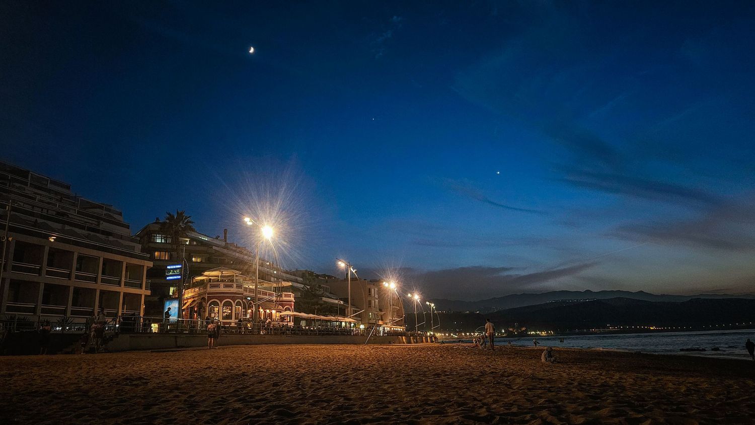 A panoramic series of coastal nighttime scenes showing beach buildings illuminated under a dark blue evening sky.