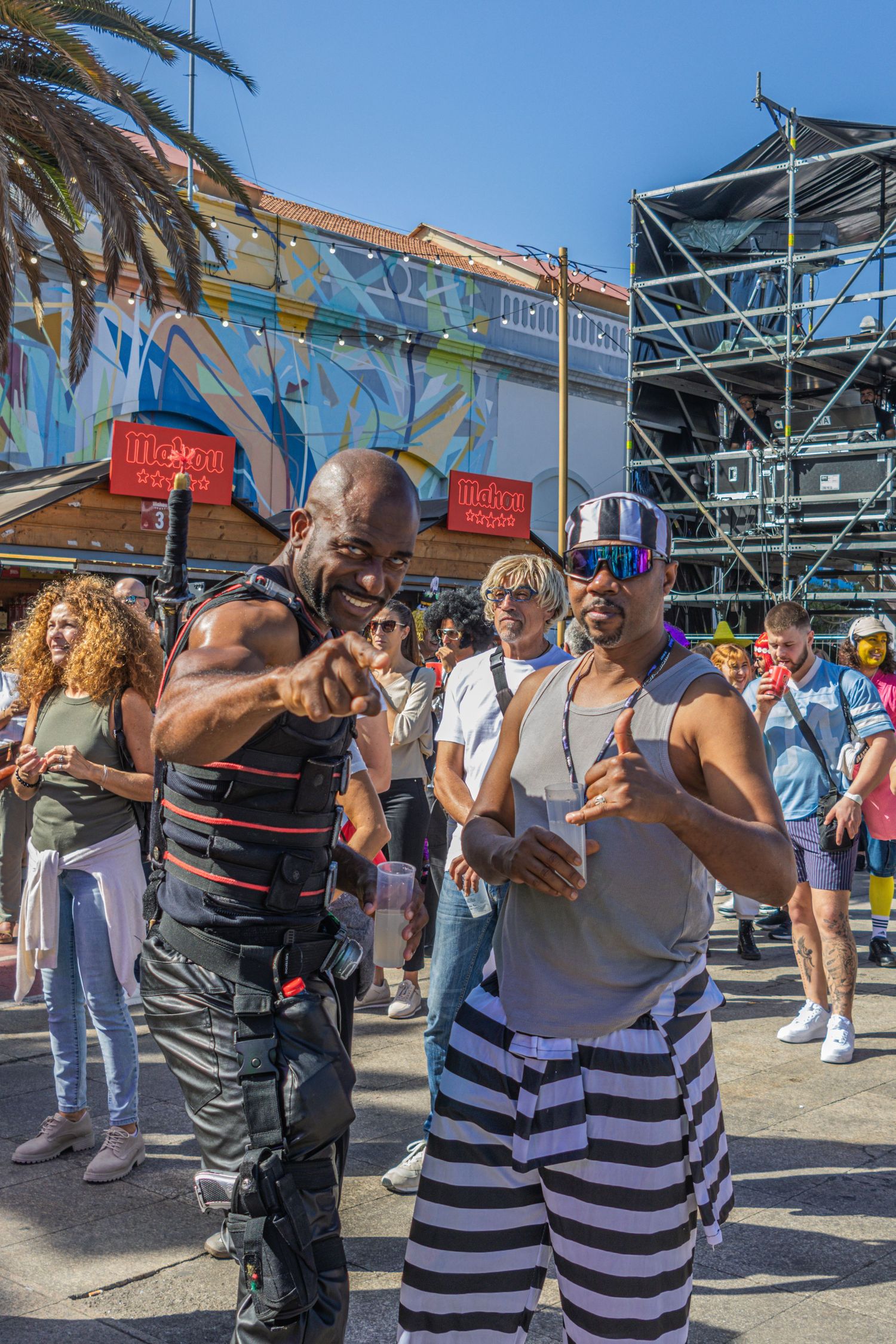 People dancing and enjoying themselves at an outdoor festival with market stalls and tents visible in the background.