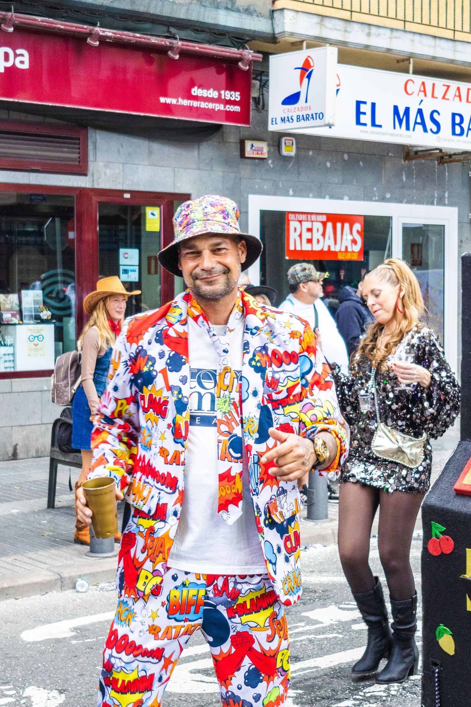 People celebrating at a street festival wearing colorful patterned clothing and festive attire outside storefronts.