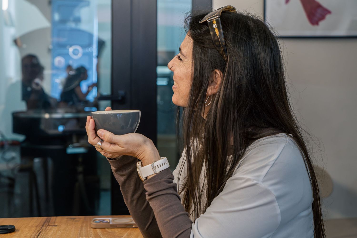 Woman sitting in a cafe holding a bowl of coffee up to her lips, enjoying a warm drink.