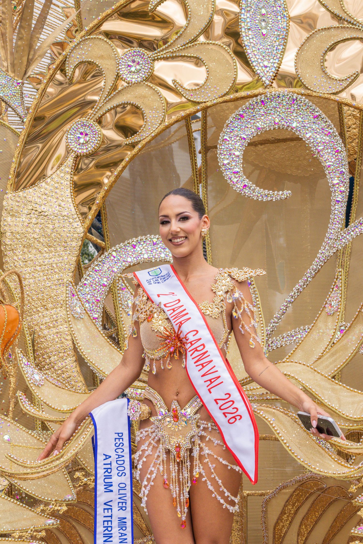 Pageant contestant wearing a sparkly costume stands in front of ornate gold and silver decorative backdrop.