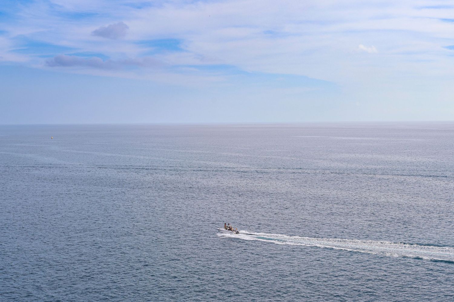 Small white boat cruising across calm blue ocean waters under bright sunny skies.